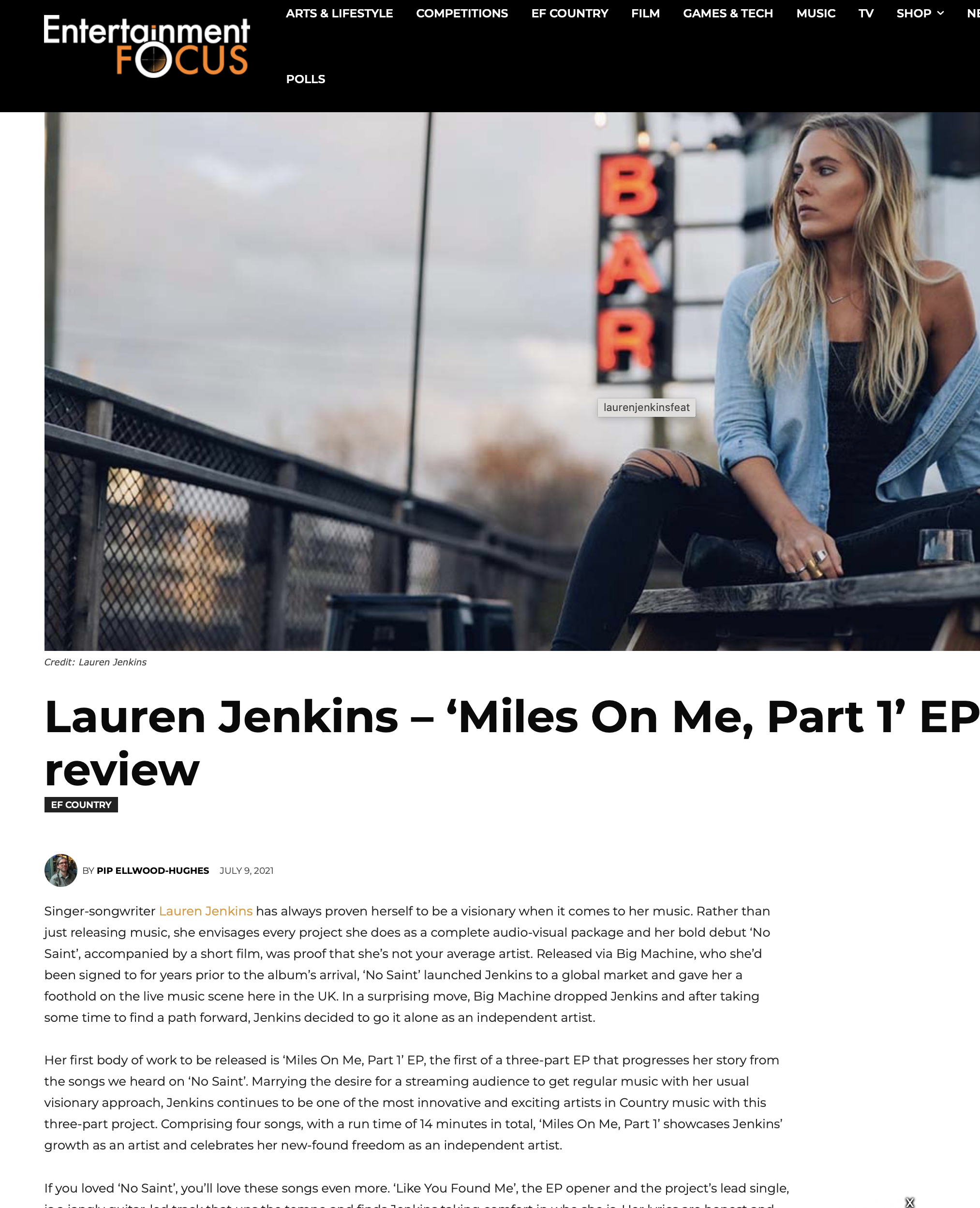 Lauren Jenkins with long blonde hair, wearing a denim jacket and black ripped jeans, sits on a wooden bench outside at dusk, with a neon sign spelling 'BAR' in the background.