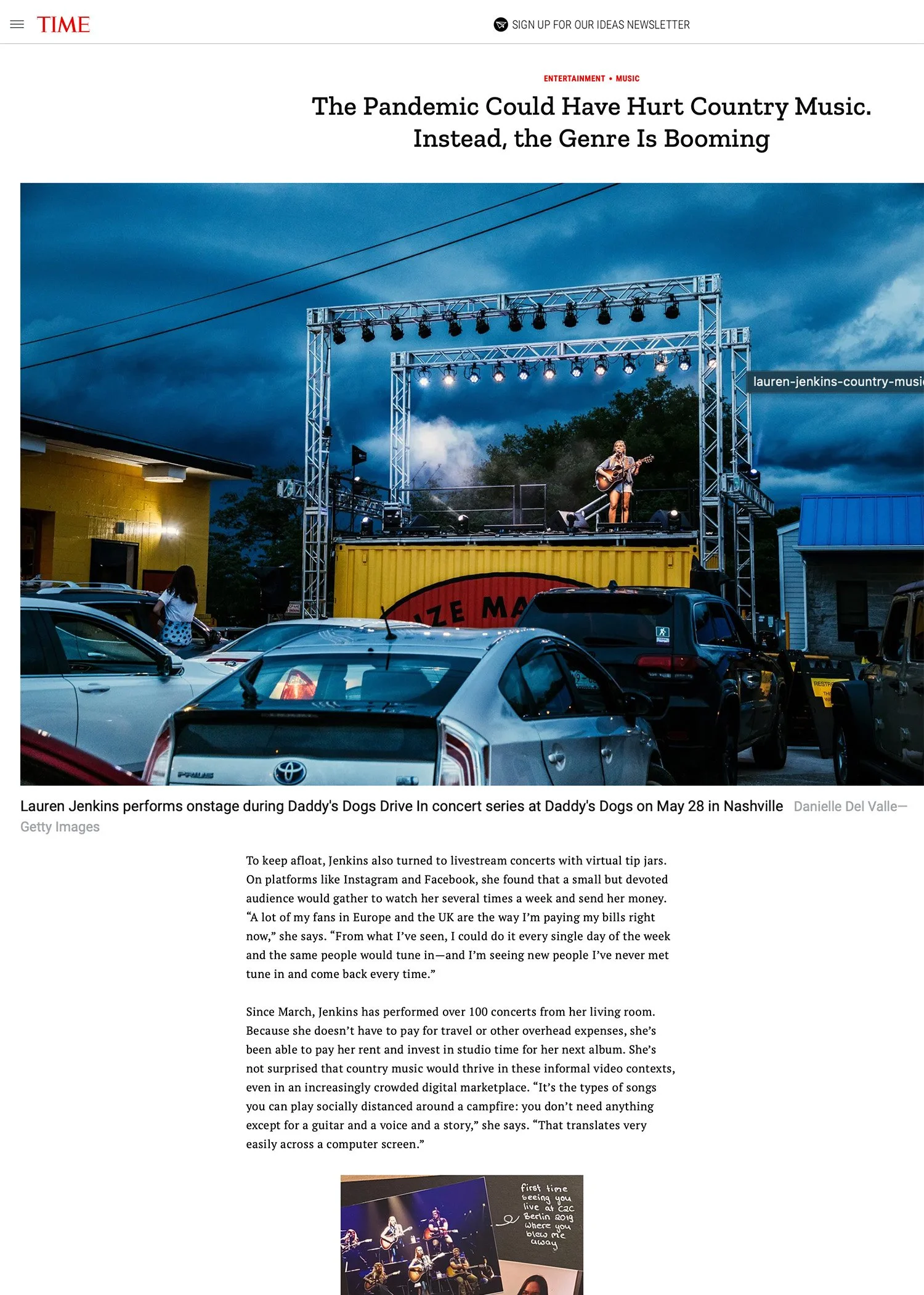 Concert stage with Lauren Jenkins performing on a truck bed stage at Daddy's Dogs Drive-In, parked cars in foreground, cloudy evening sky.
