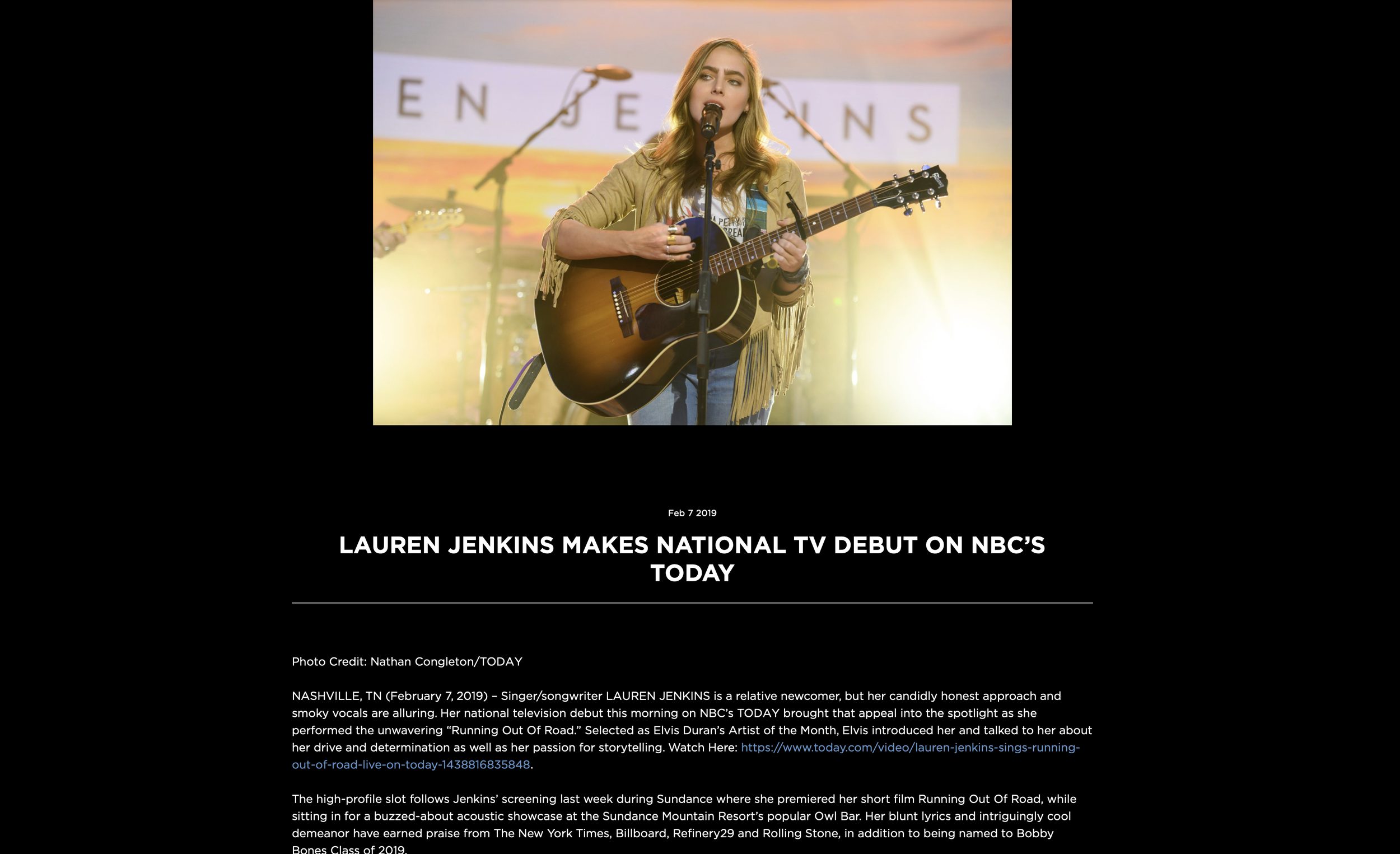 Young woman, Lauren Jenkins with long blond hair performing with an acoustic guitar on stage, microphone in front, microphone stand, and sunset backdrop with letters in the background.