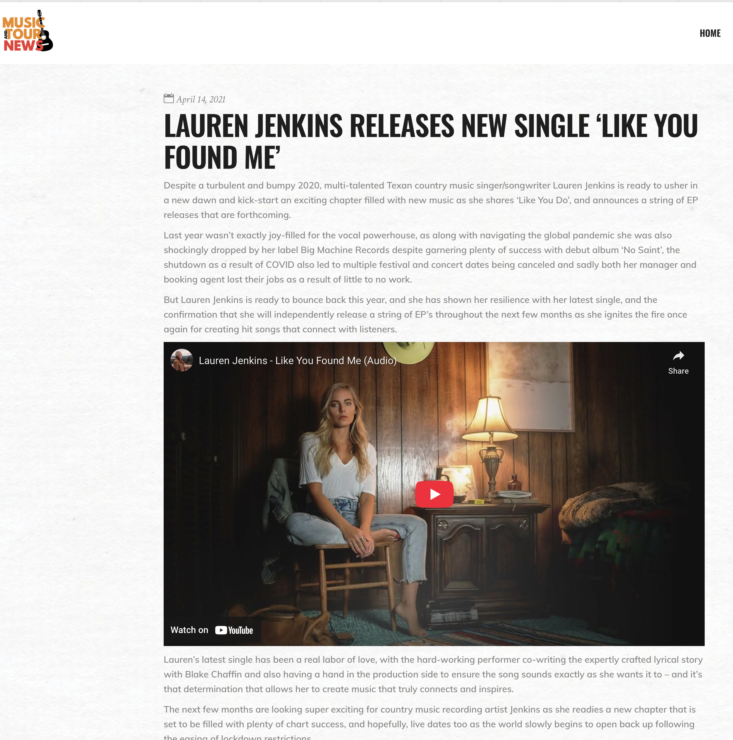 Lauren Jenkins with long blonde hair, wearing a white top and jeans, sitting on a small stool in a cozy, dimly lit room with wooden walls, a table lamp, and a blanket on a bed behind her.