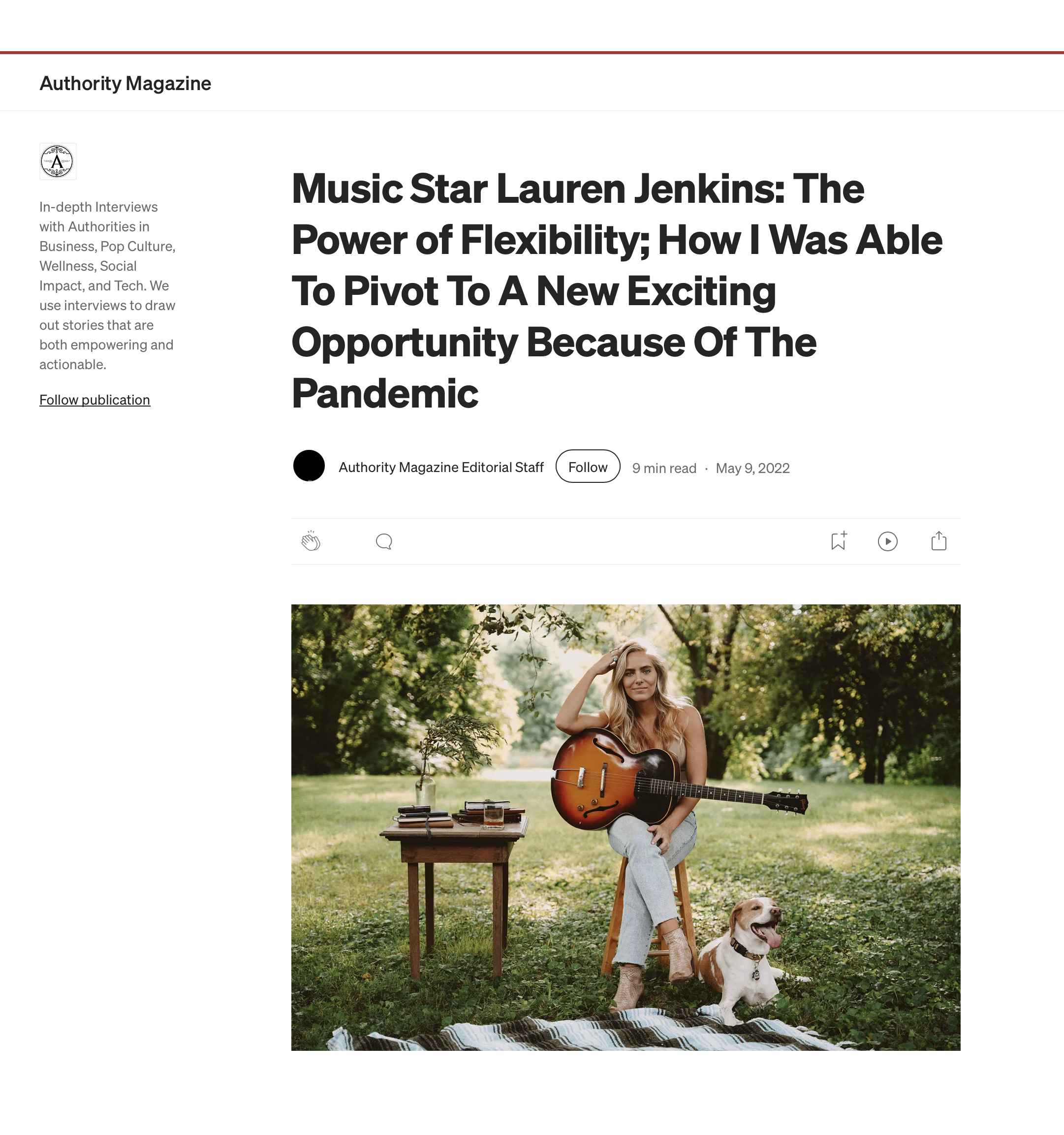Lauren Jenkins sitting outdoors on a wooden chair holding an acoustic guitar, with a dog lying on a blanket nearby, set in a lush park during daytime.