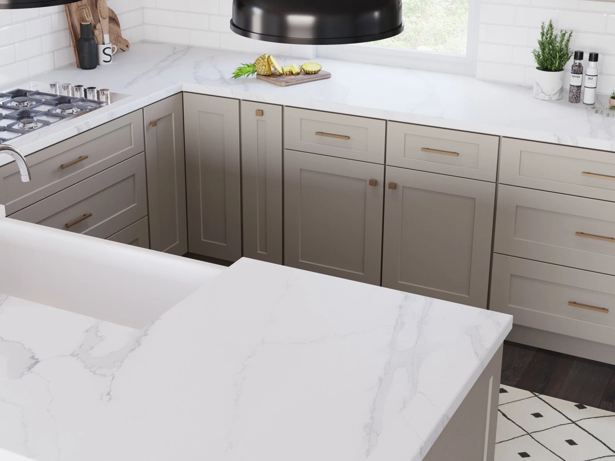 Modern kitchen with white marble countertops, beige cabinets, and a gas stove. Decor includes cutting boards, spices, and a plant. A black pendant light hangs above and natural light streams through a window.