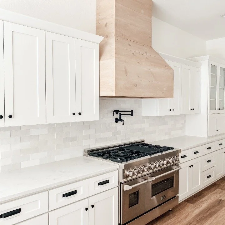Modern kitchen with white cabinets, stainless steel stove, and wooden range hood