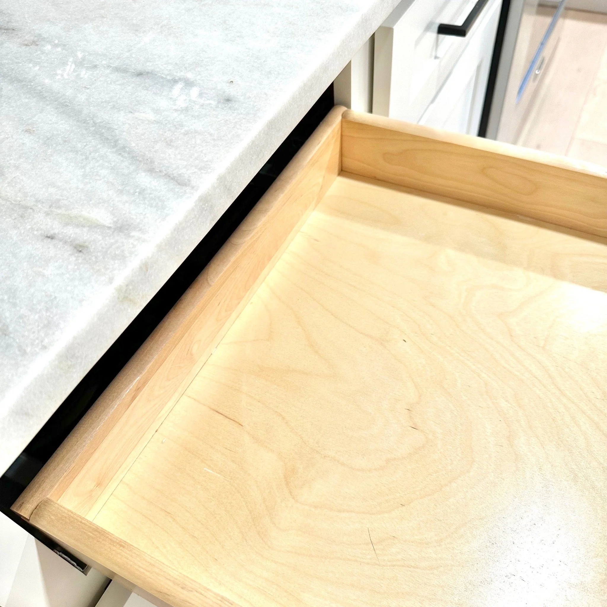 Wooden drawer under a white marble countertop, partially open