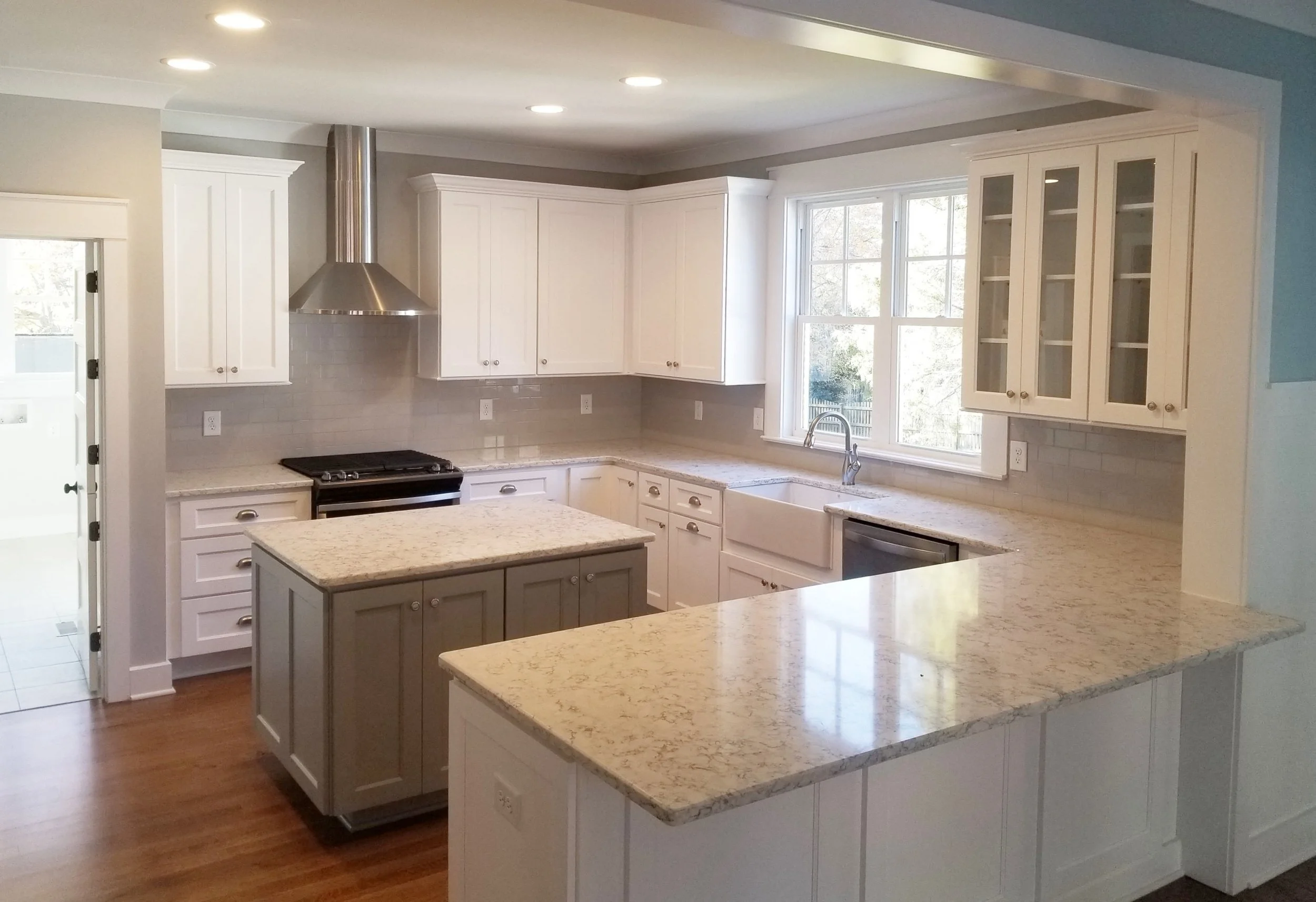 Modern kitchen with white cabinets, granite countertops, stainless steel appliances, and a large window.
