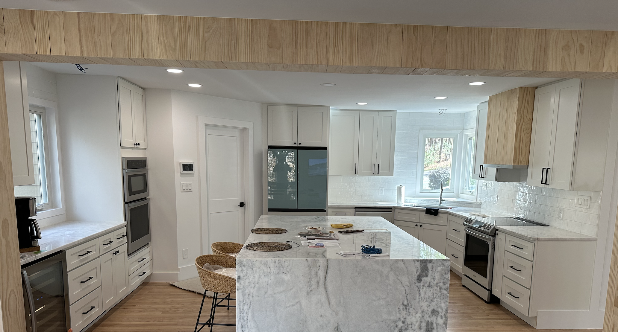 Modern kitchen with white cabinets, marble countertops, stainless steel appliances, and a kitchen island with woven stools.
