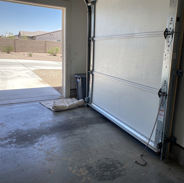 Interior of an open garage with concrete floor showing white door and driveway beyond with desert landscaping.