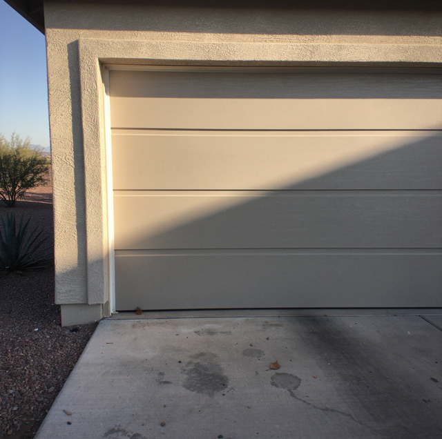 A two-car garage door with horizontal panels mounted on a textured concrete wall beside a concrete driveway.