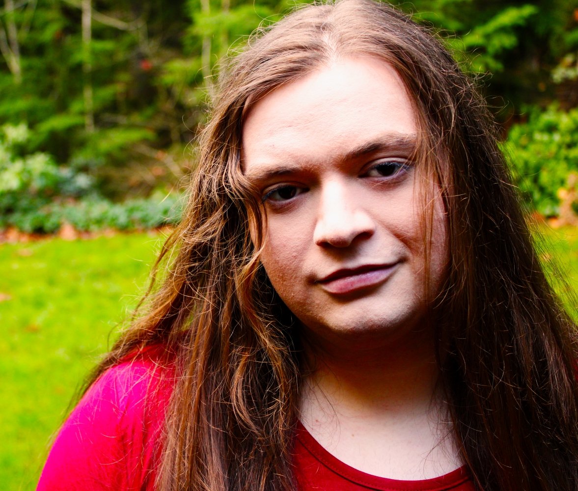Person with long hair wearing a red shirt in a green outdoor setting.