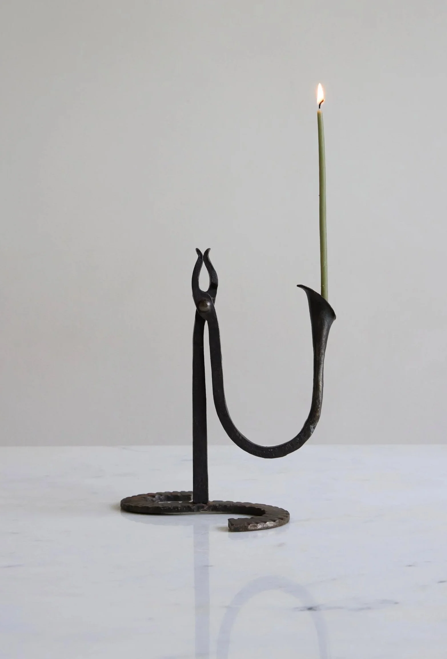 A metal candle holder with a spiral base holding a single lit matchstick candle.
