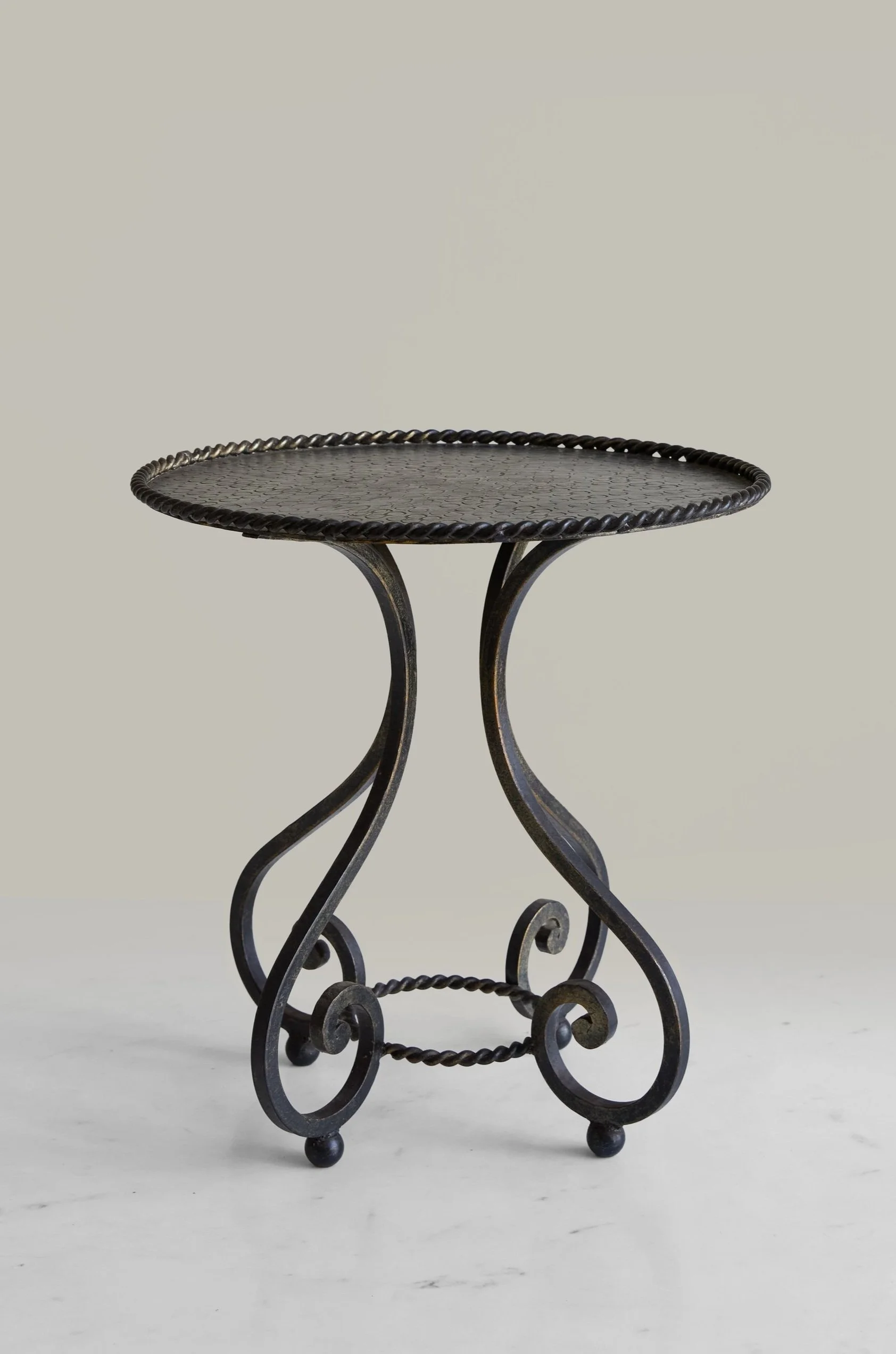 Black wrought iron side table with a round top and ornate curved legs on a light-colored surface.