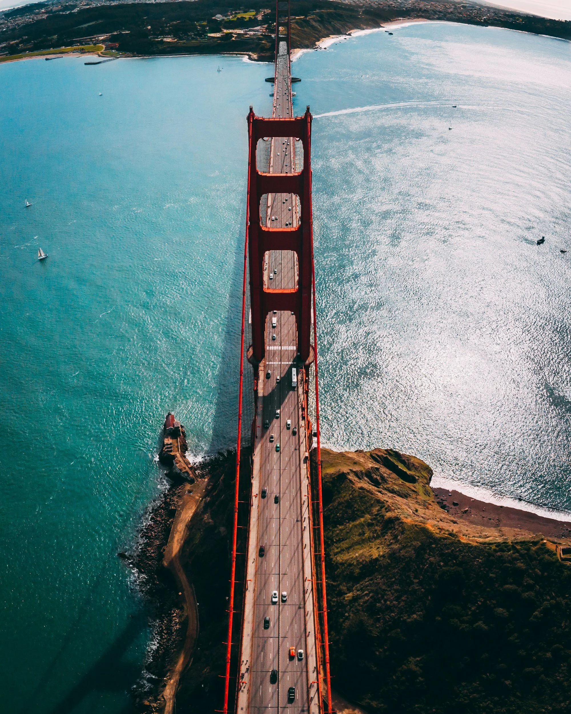 Aerial view of the Golden Gate Bridge crossing San Francisco Bay with cars traveling on the bridge and sailboats in the water below.