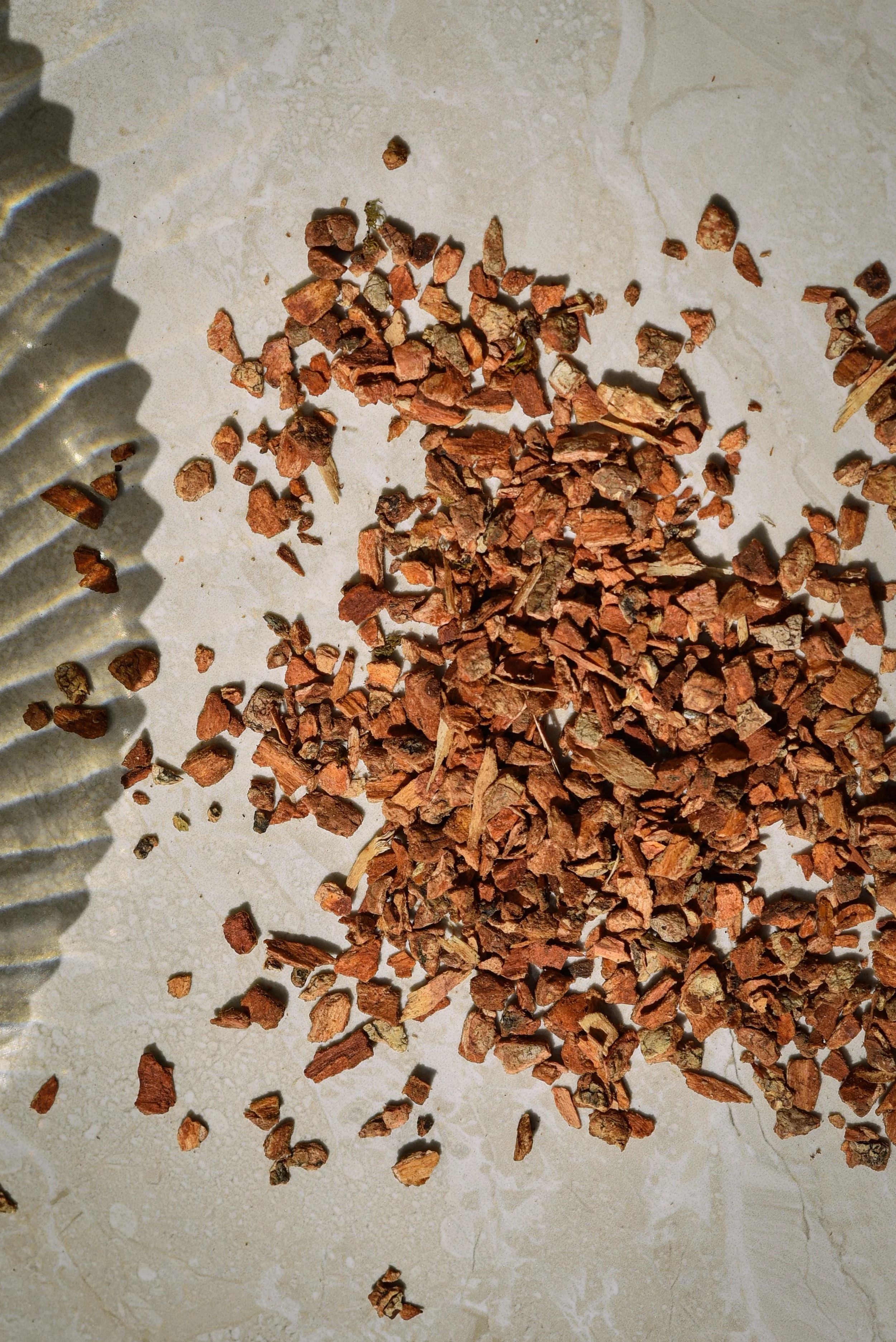 Small, reddish-brown crushed stones and fragments scattered on a light-colored surface, with a metal tool partially visible on the left side.