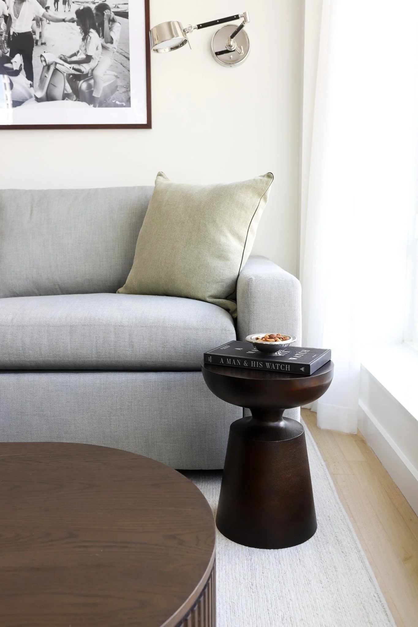 Close-up vignette of a luxury gray sofa corner paired with a custom wood side table styled with a book and a small bowl.