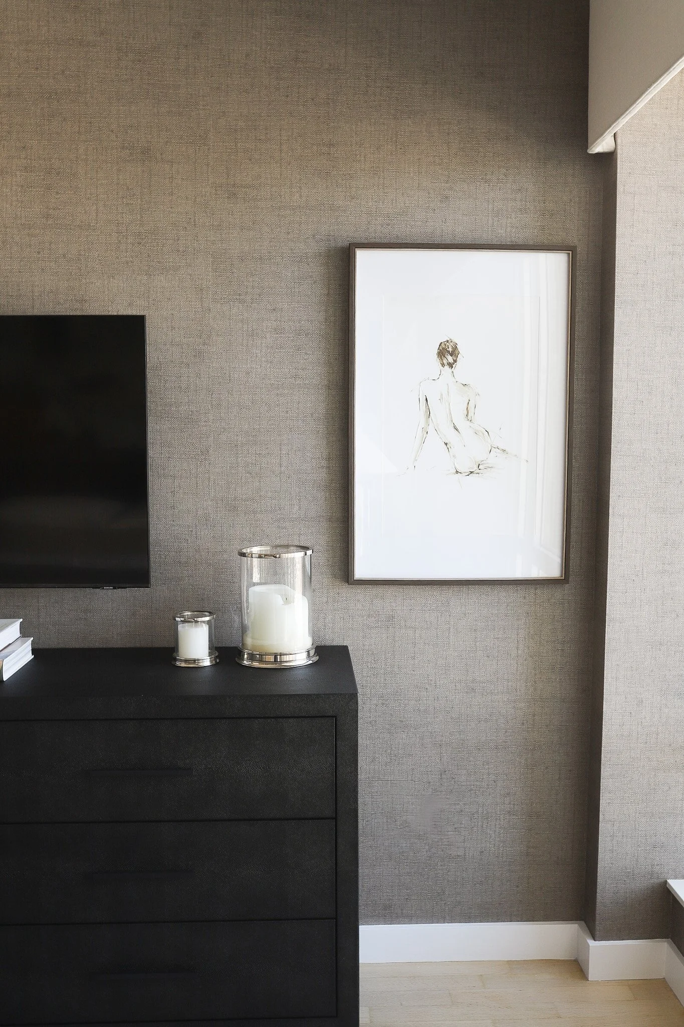 Corner of a luxury living room showcasing a textured accent wall with framed artwork next to a custom dark wood TV stand and candle decor