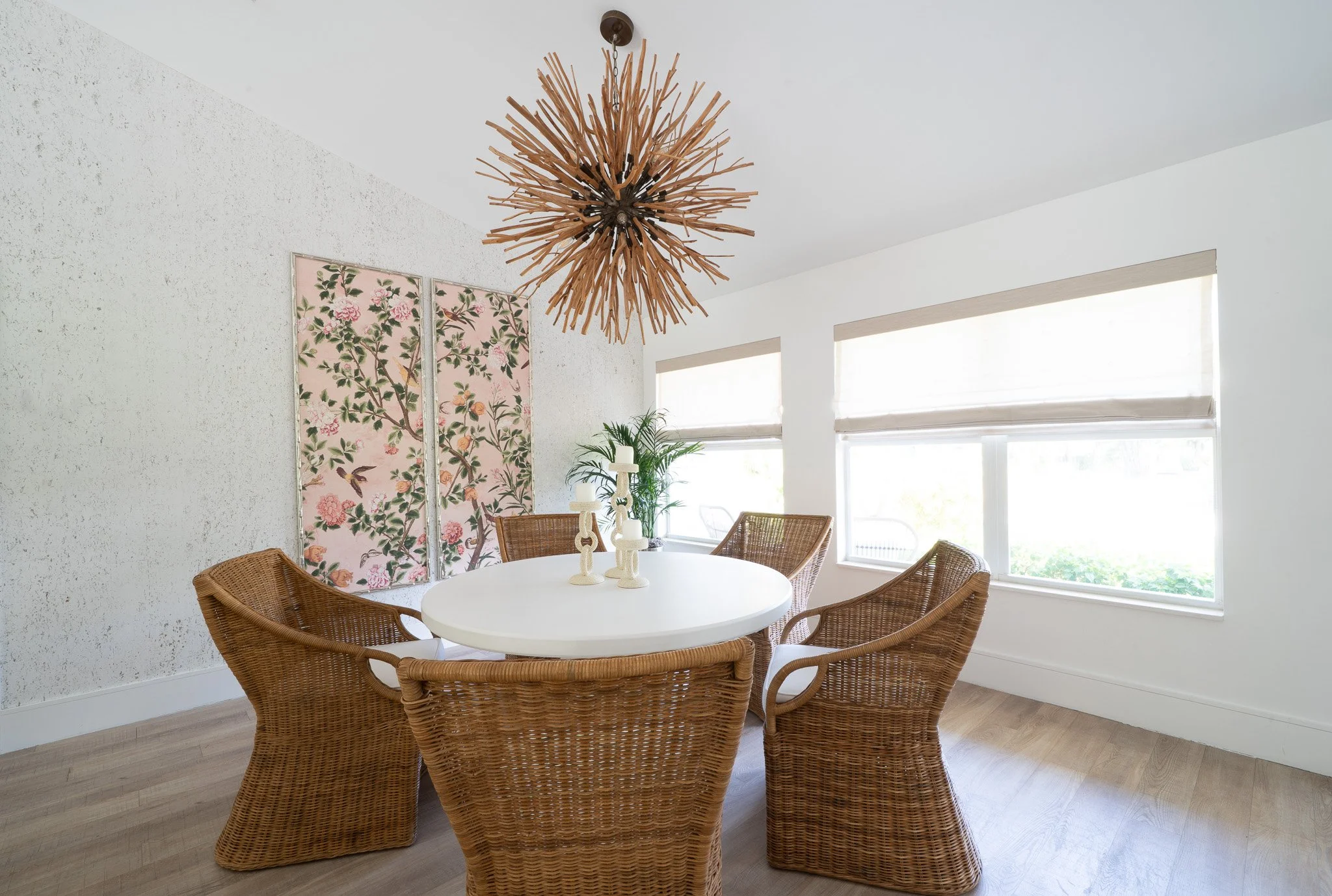 Alternate angle of a modern coastal dining room showcasing woven chairs around a stone table next to a wall of windows letting in bright natural light.