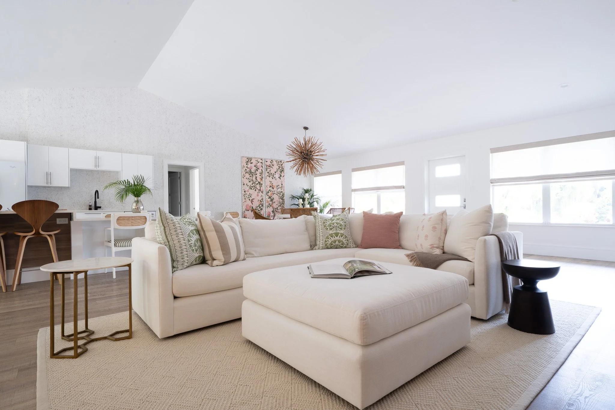 Bright living room with a cream performance fabric L-shaped sectional couch, matching square ottoman, cream rug, and dark wood side table on hardwood floors.