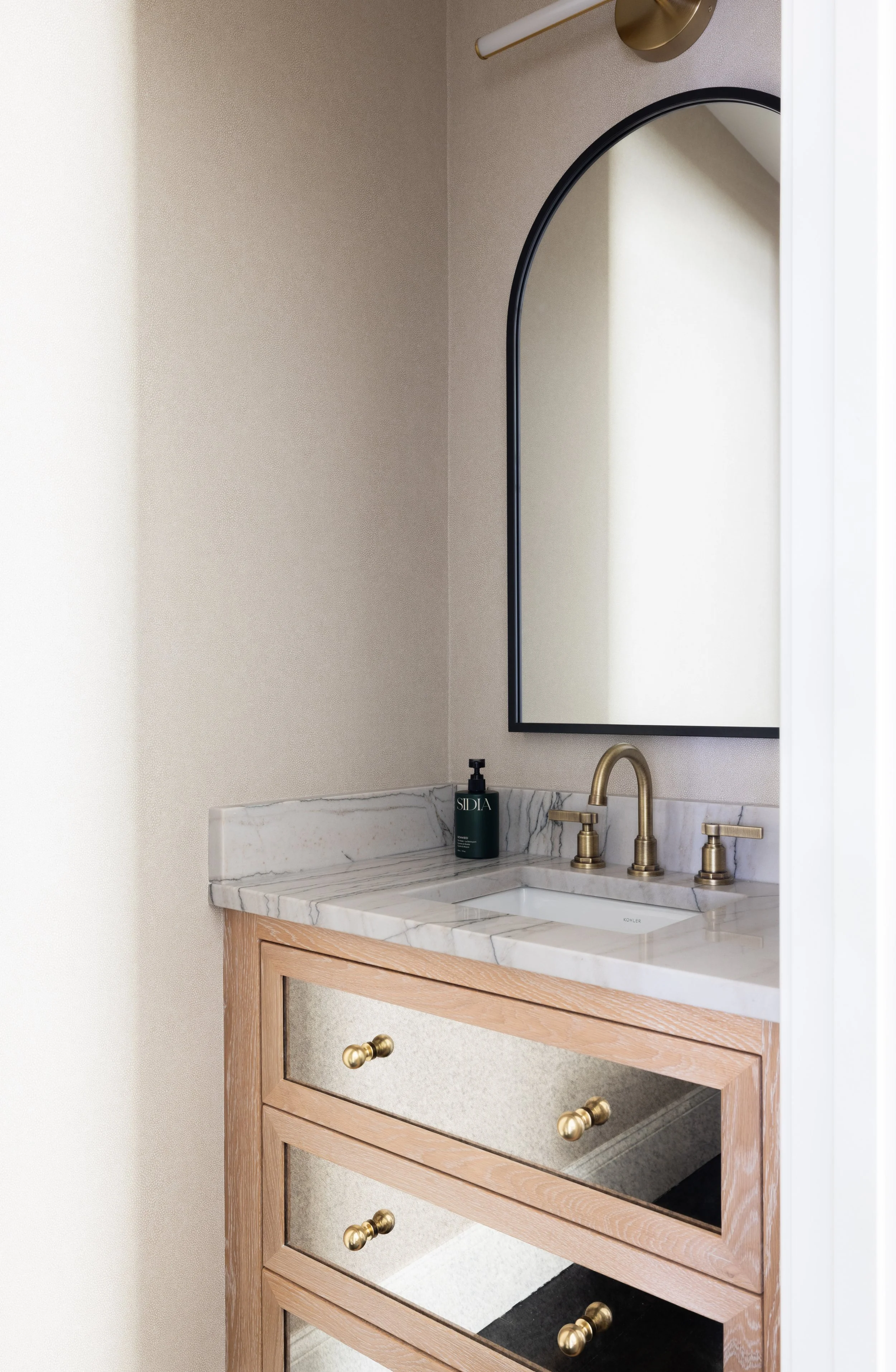 Angled view of a guest bathroom vanity highlighting a marble integrated sink, warm gold faucet fixtures, and custom modern cabinetry.
