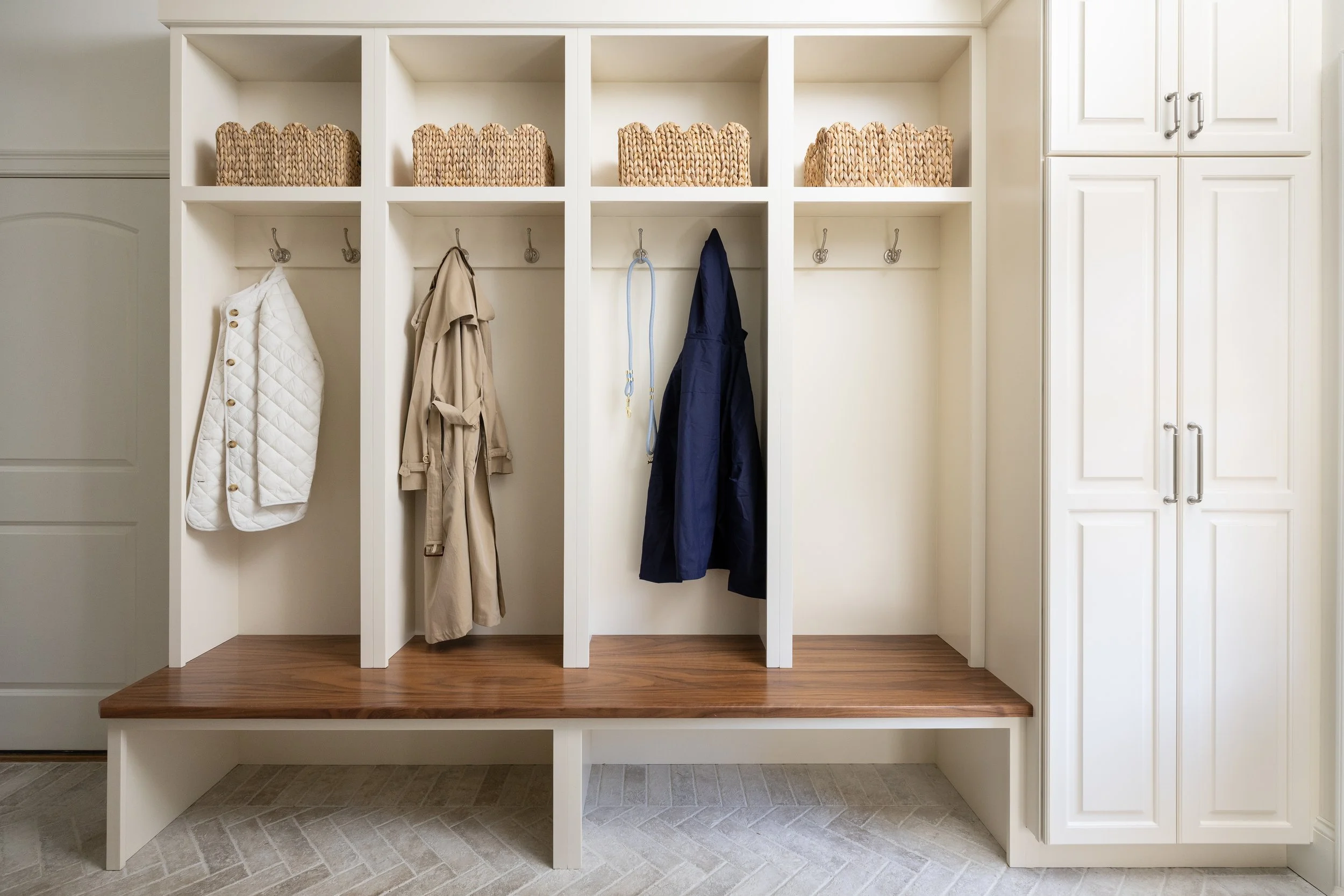 White built-in mudroom storage with hooks holding coats and a basket on top shelf