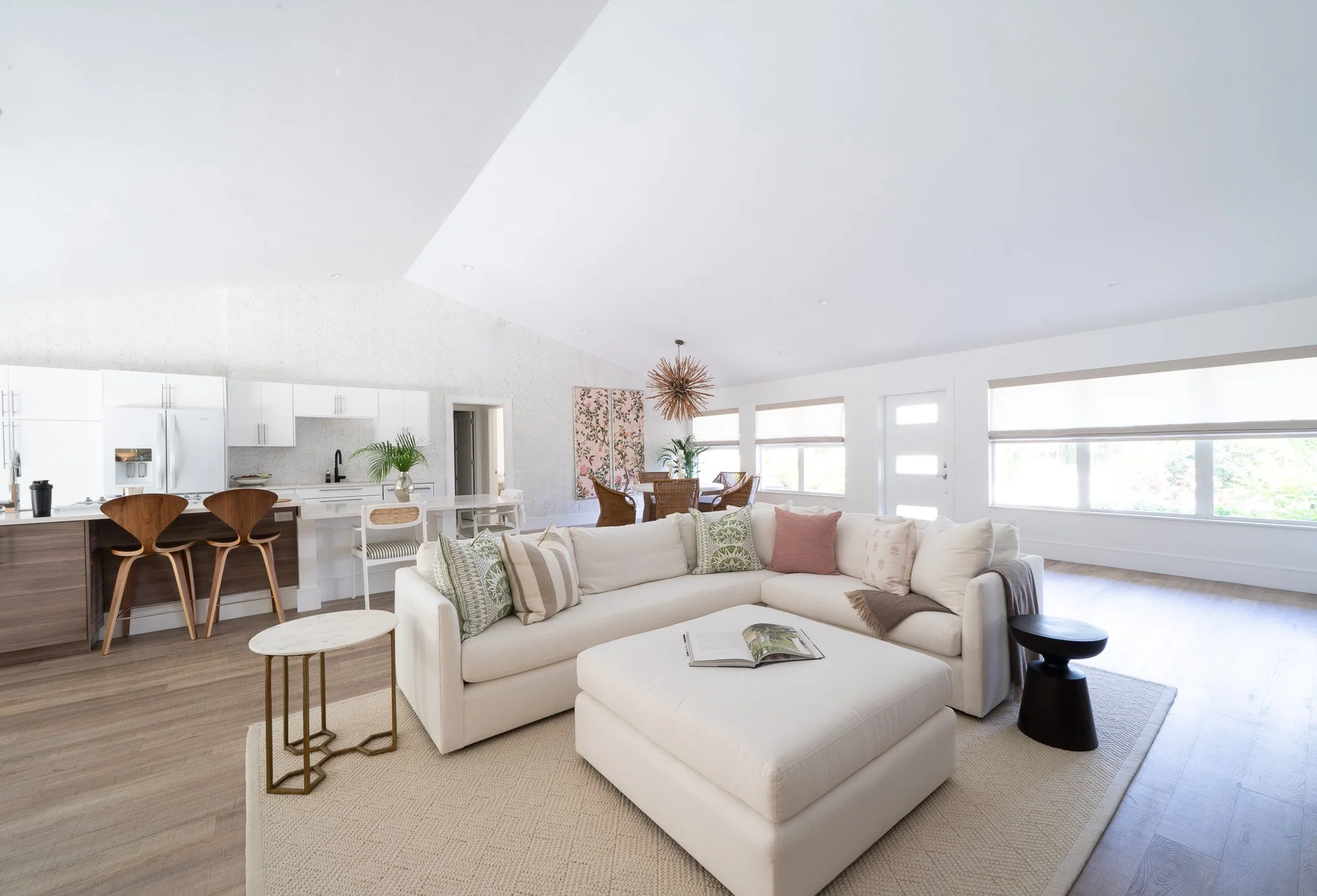 Expansive wide shot of a luxury open-floor-plan condo showing the living area, dining set, and white kitchen framed by a wall of windows.