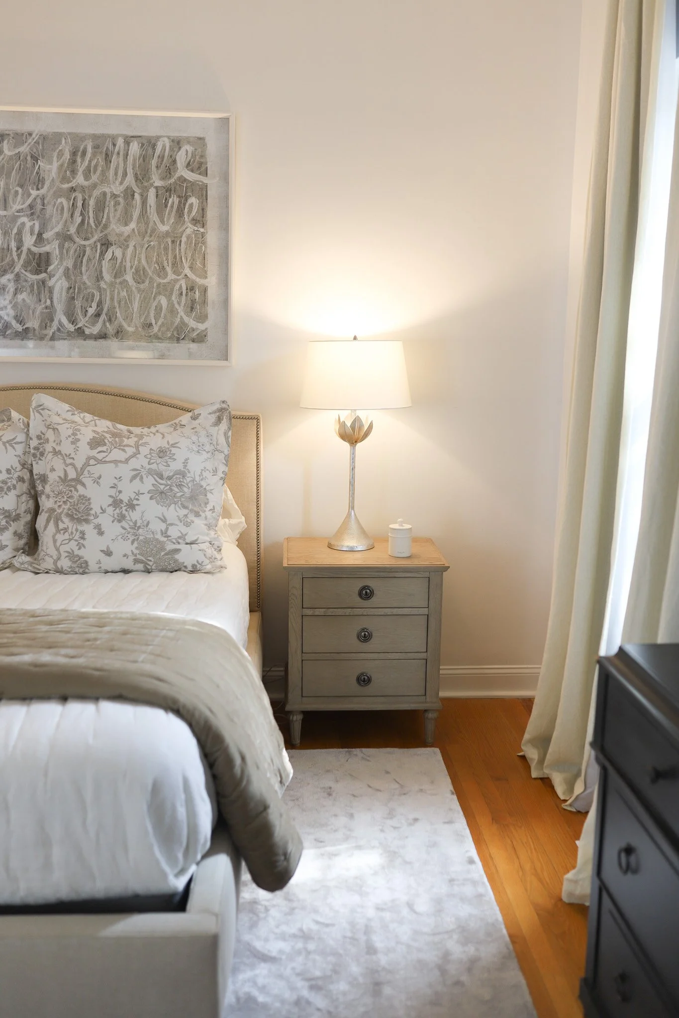 Bedroom with white and brown beddings, floral pillow cases, contemporary art and warm, flower-accent bedside lamp