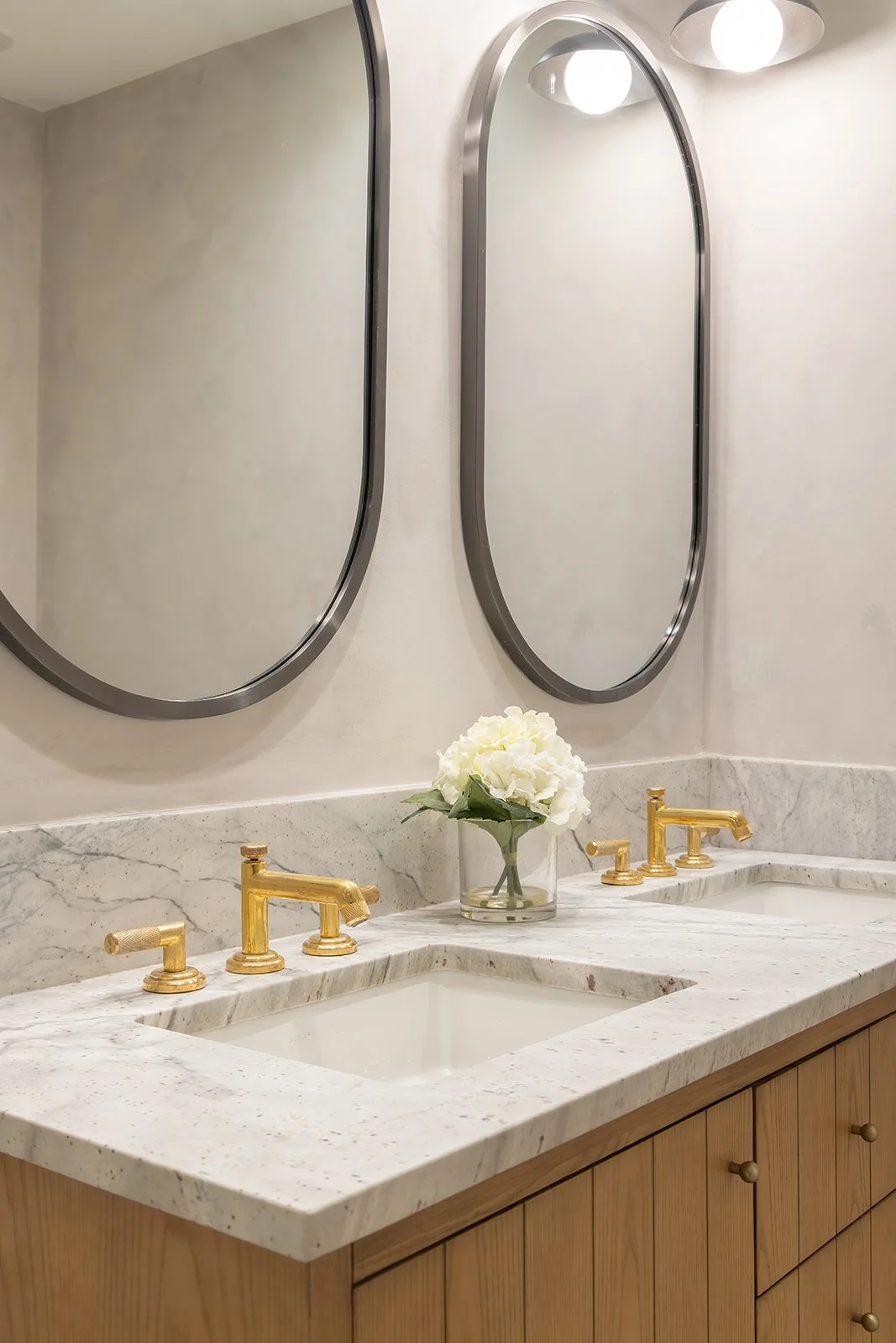 Side-angle close-up of a modern bathroom sink detailing a light marble vanity surface and sleek gold plumbing fixtures.