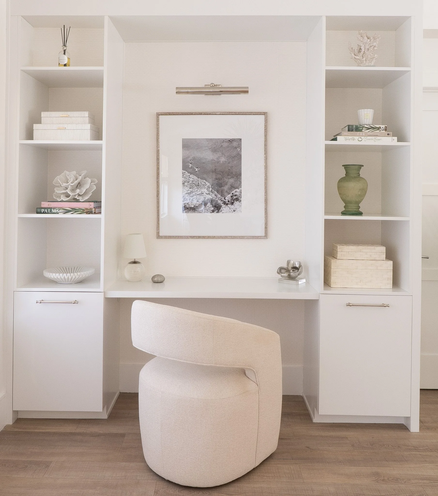 Custom home office nook featuring high white built-in shelving, a modern design studio chair, overhead lighting, and framed artwork.