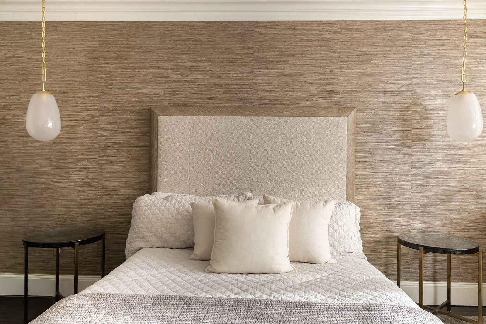 Symmetrical front view of a master bed flanked by matching dark glass bedside tables and elegant hanging gold pendant lights.
