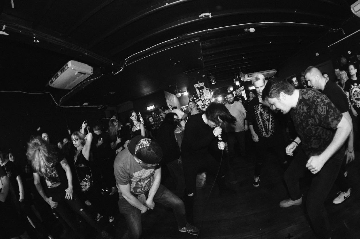 Black and white photo of a live music concert with a singer holding a microphone, and a crowd dancing and enjoying the performance in a dimly lit indoor venue.
