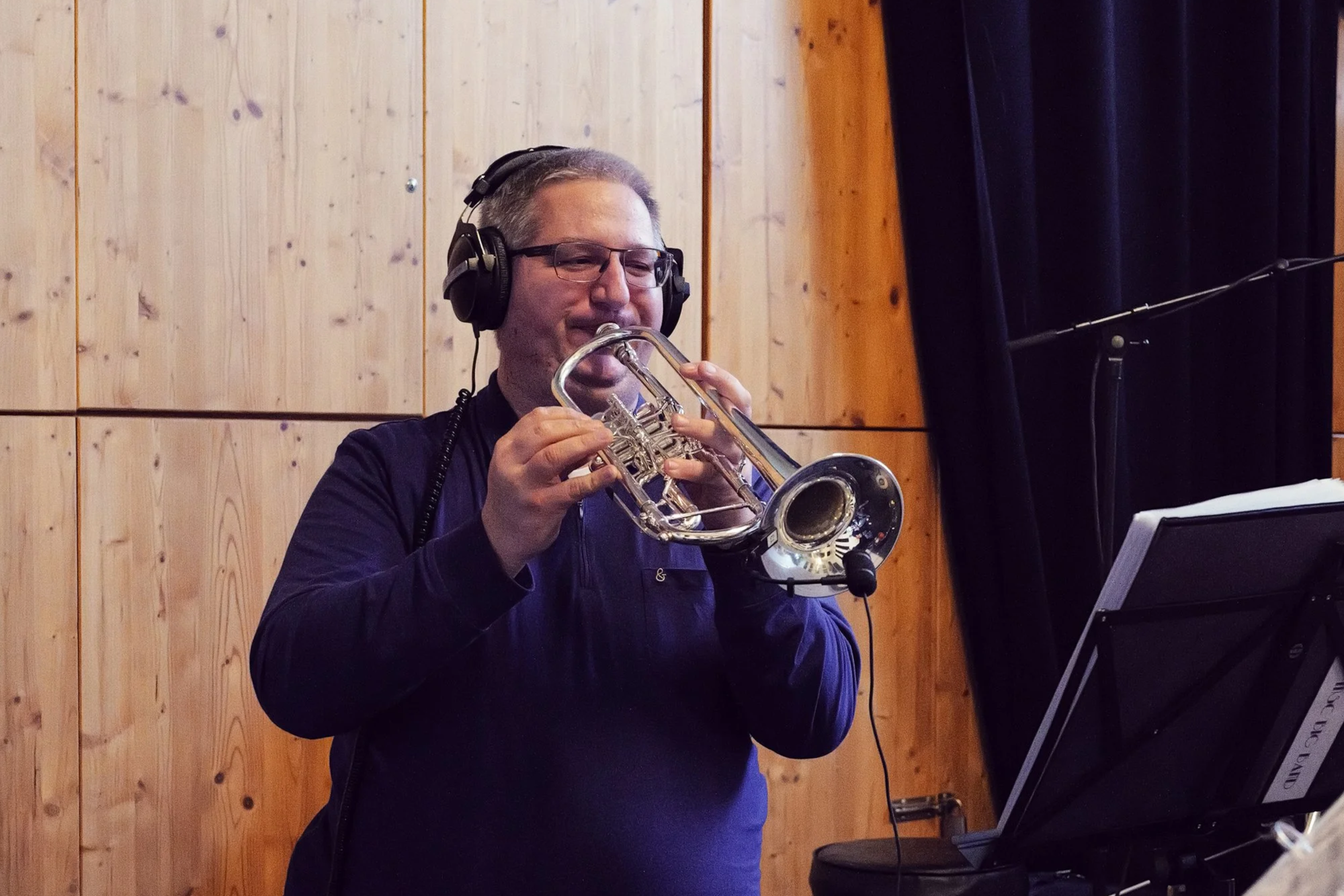 Ein Mann mit Kopfhörern spielt auf einer Silber-Trompete in einem Aufnahmestudio.