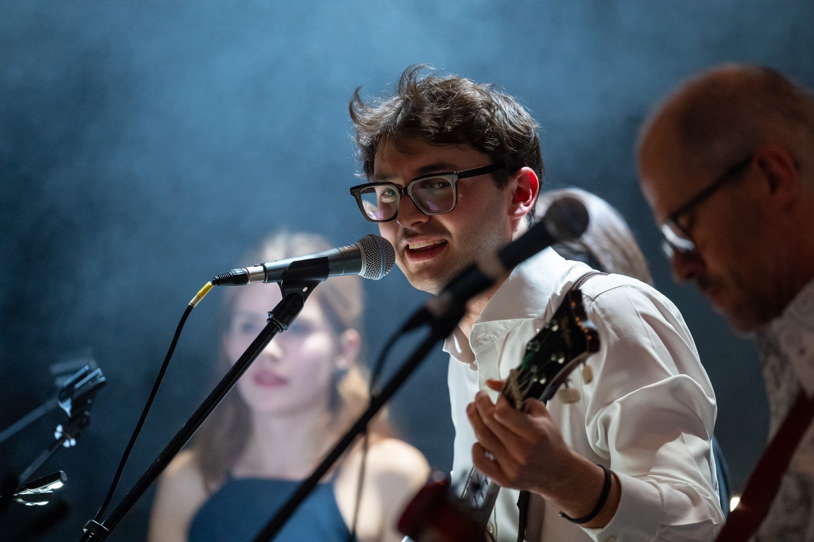 Ein junger Mann spielt Gitarre und singt auf einer Bühne mit roten Vorhängen.