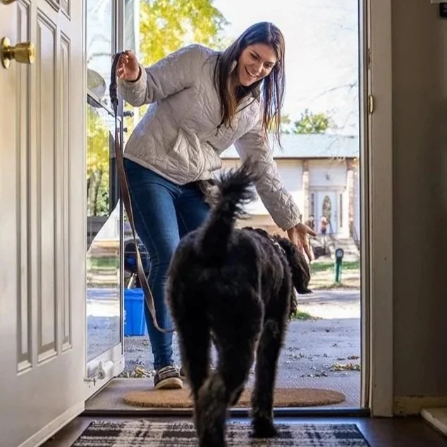 A female professional dog trainer with a dog at the front door.