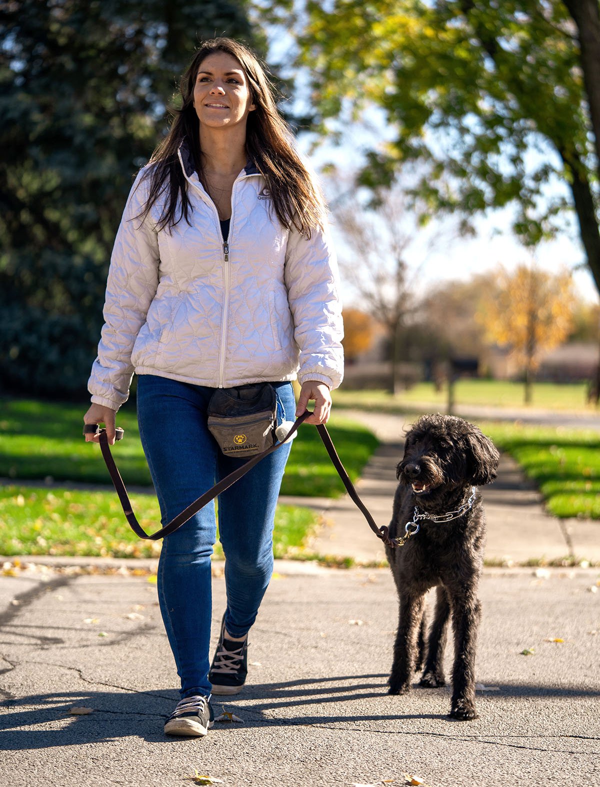 Woman walking a black dog in a sidewalk.