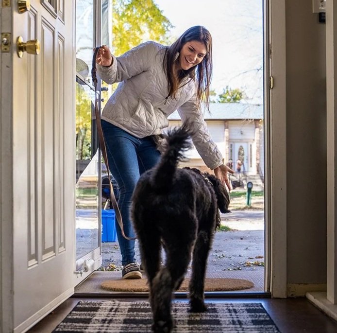 Trainer greeting a black dog at the doorway at the start of a training day.