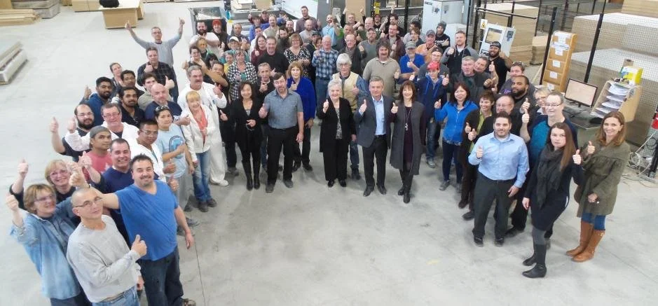 Group of people gathered in a warehouse, posing for a photo with many giving thumbs up.