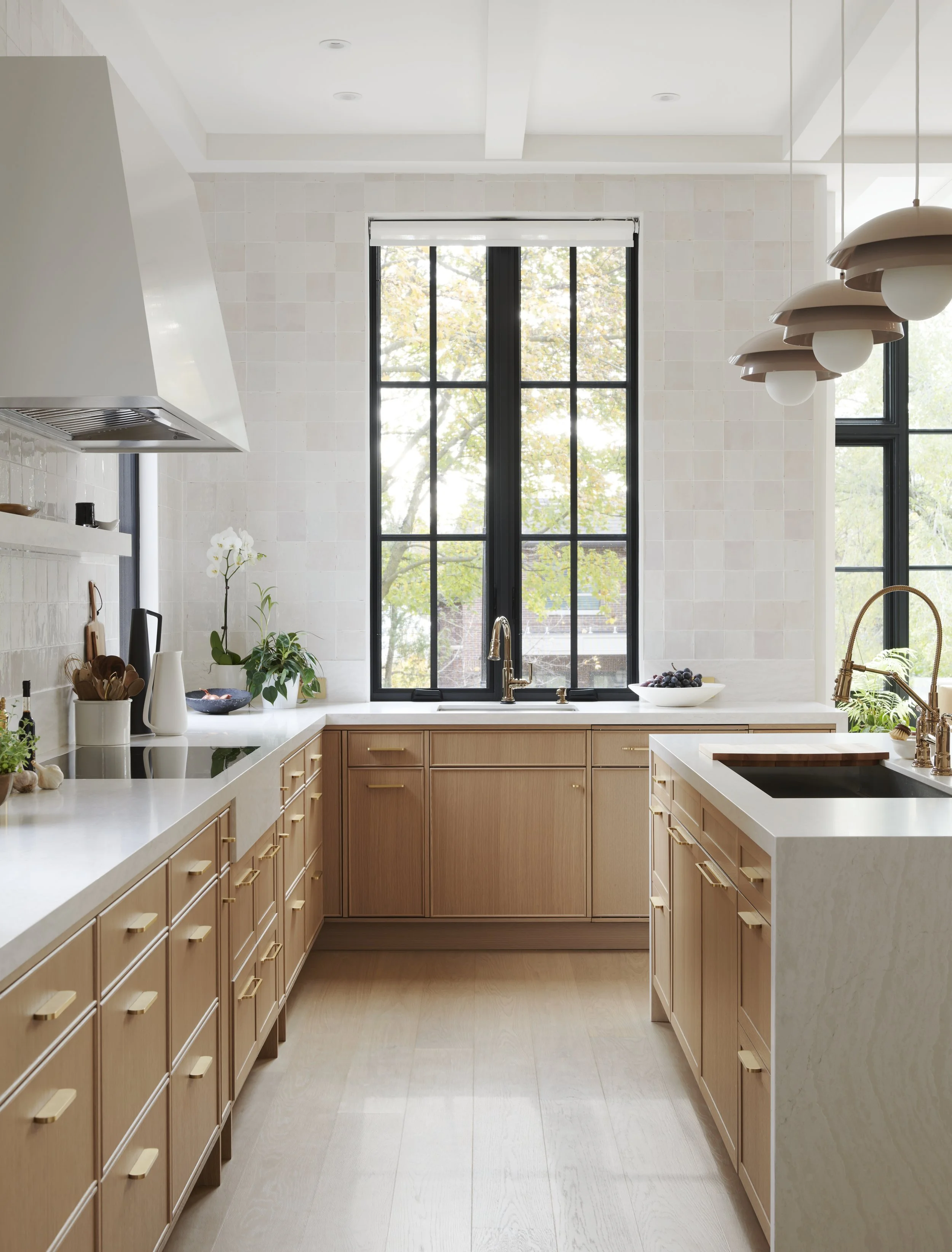 Modern kitchen with large windows, light wood cabinetry, white countertops, and a black sink.