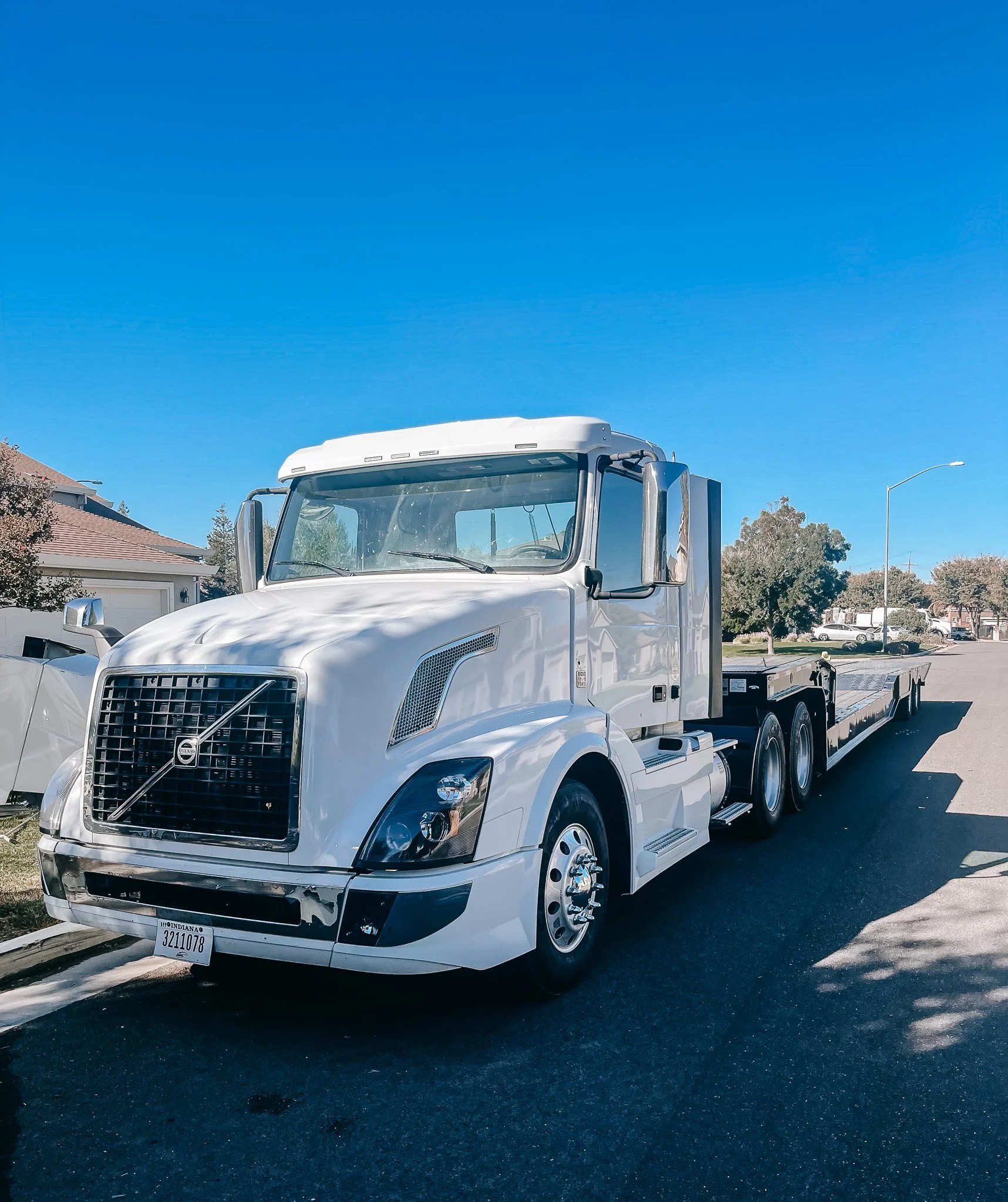 White flatbed truck parked on a residential street under a clear blue sky.