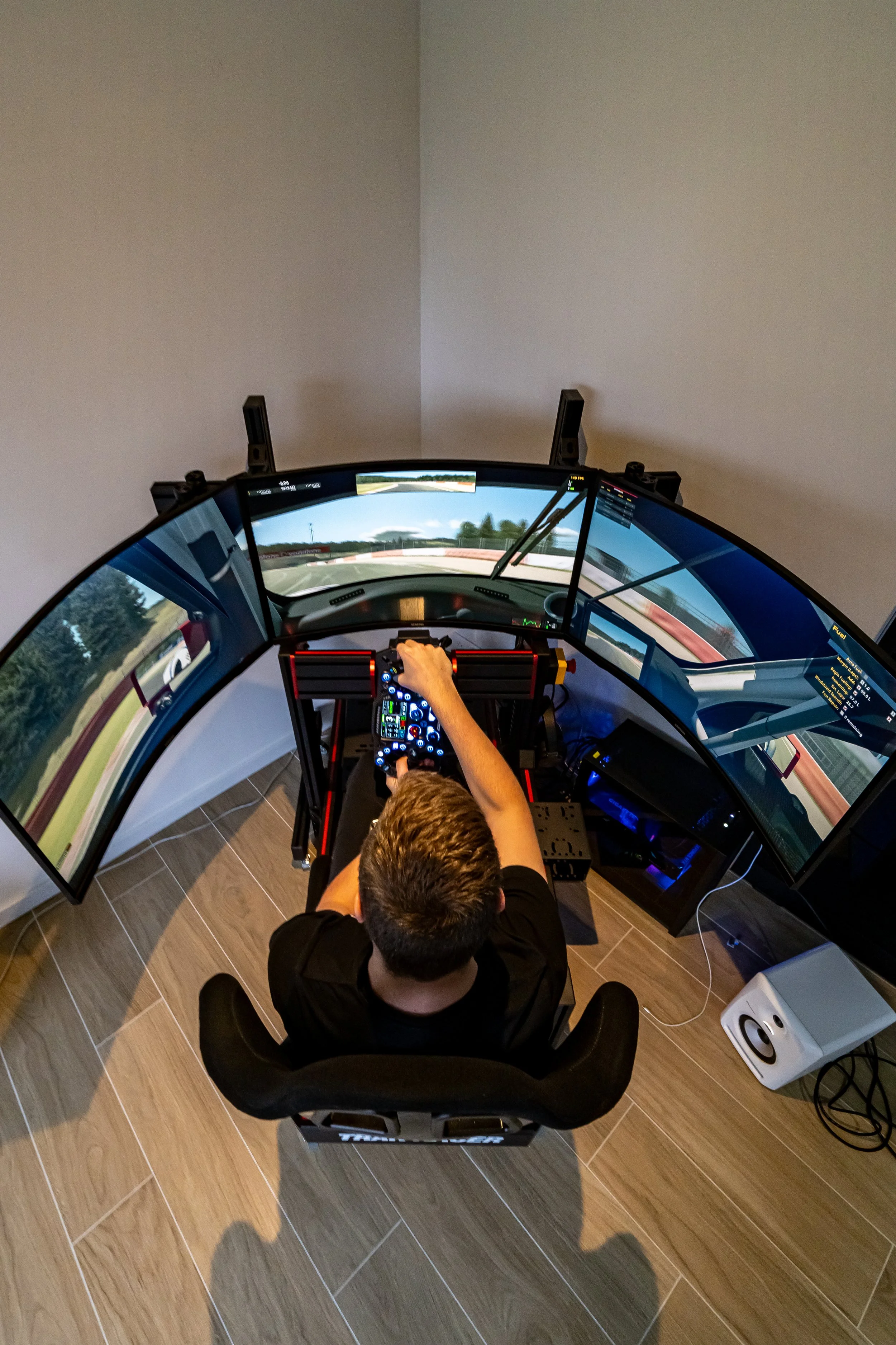 Persoon die een race-simulatieset gebruikt, bestaande uit meerdere schermen en een stuureenheid, in een kamer met houten vloer.