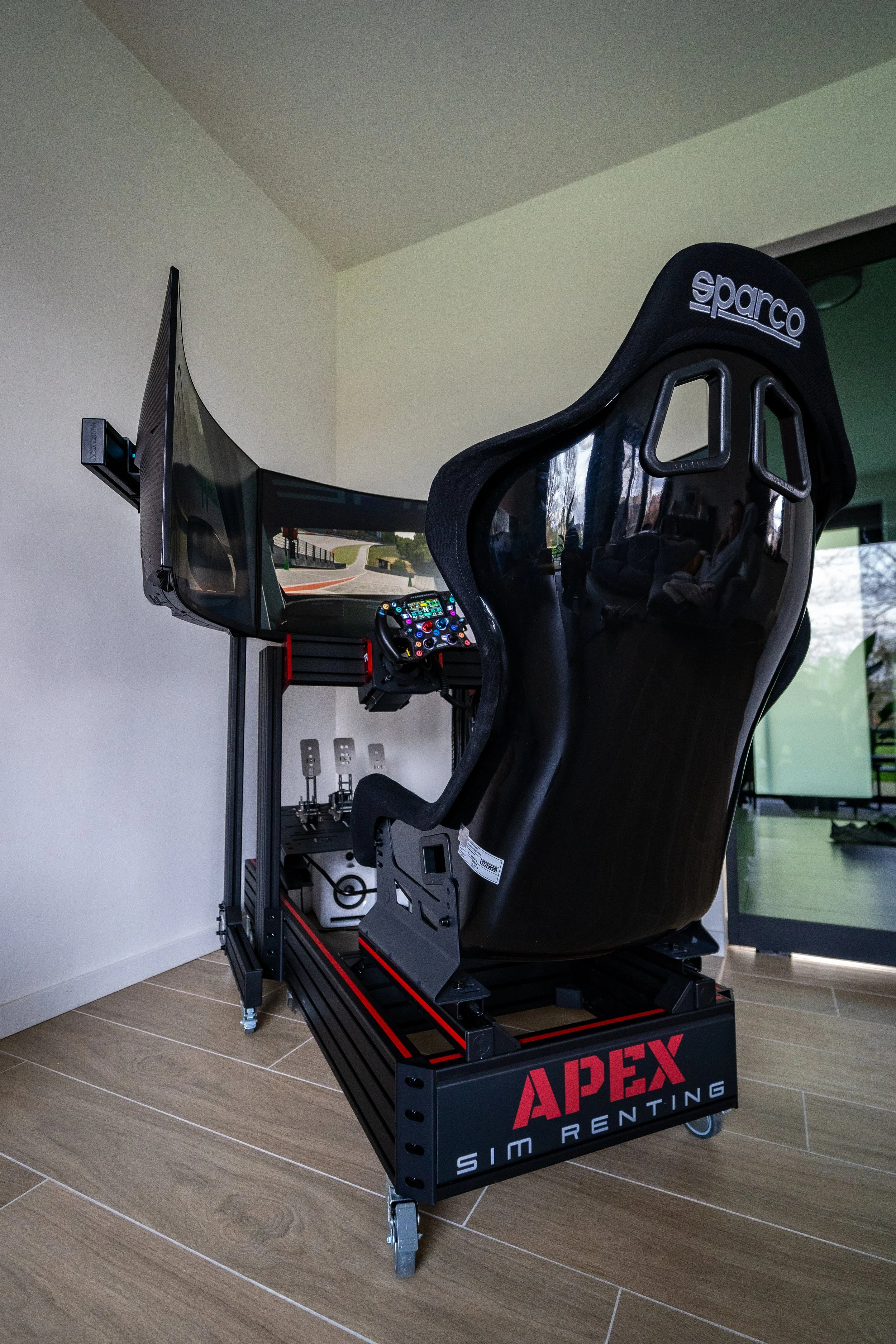 Een rallysimulatorkap met een racestoel en stuurwiel, geplaatst op een platform met wieltjes voor simracetraining.