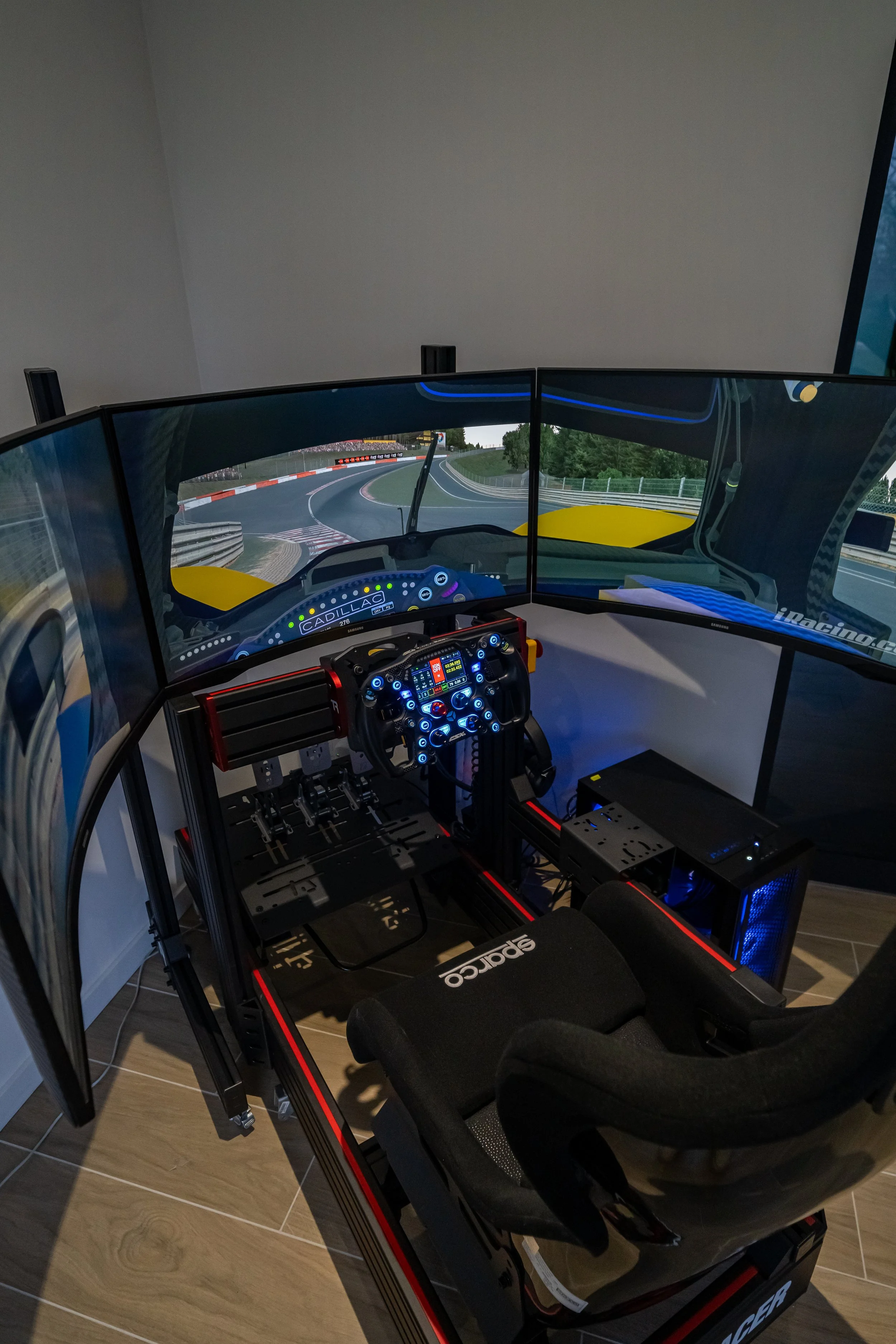 Racing simulator met drie schermen, racestoel en stuur, geplaatst in een kamer.