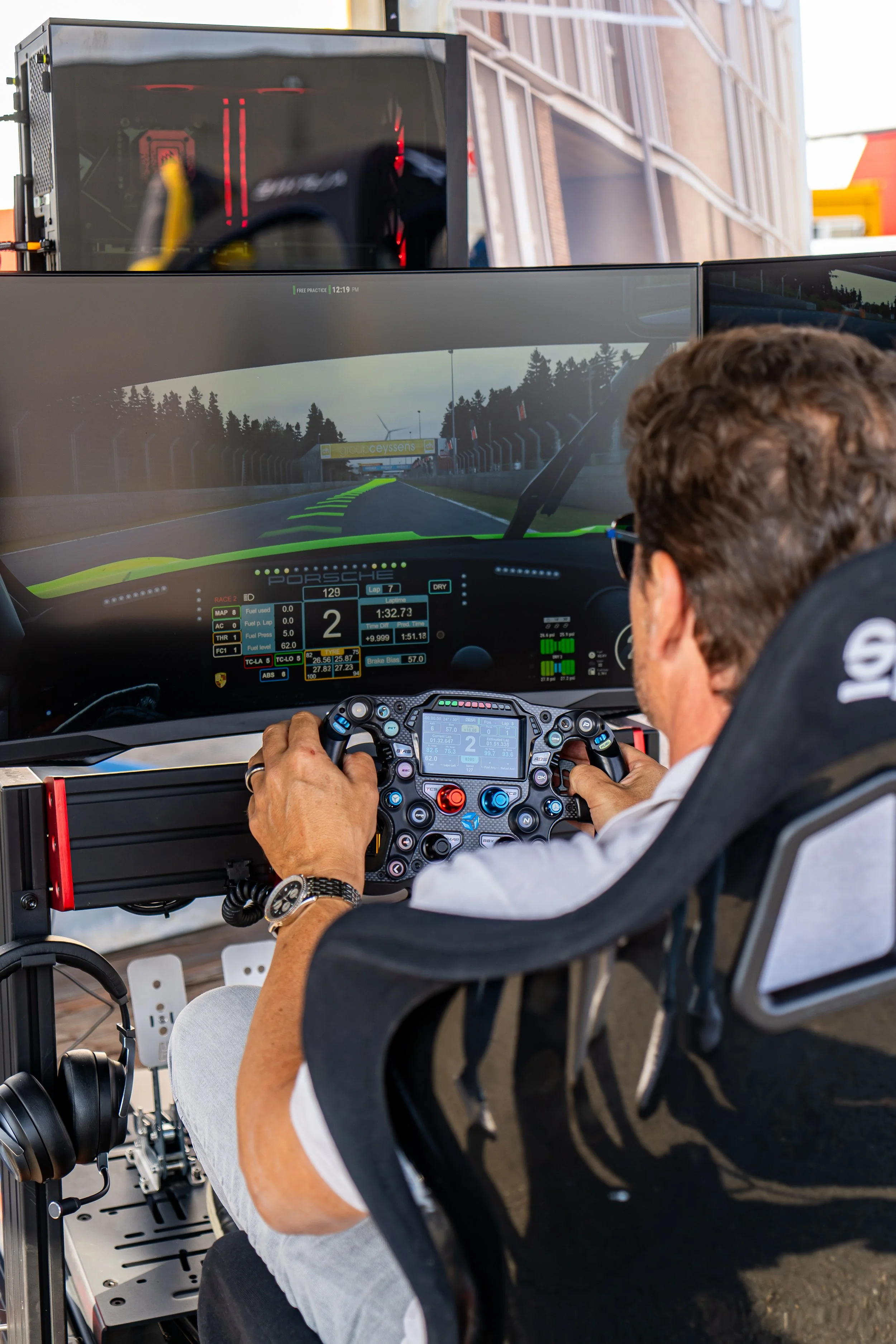 Man in een racestoel die een scherm bedient, met een virtuele raceauto en de racetrack zichtbaar op een monitor voor hem.