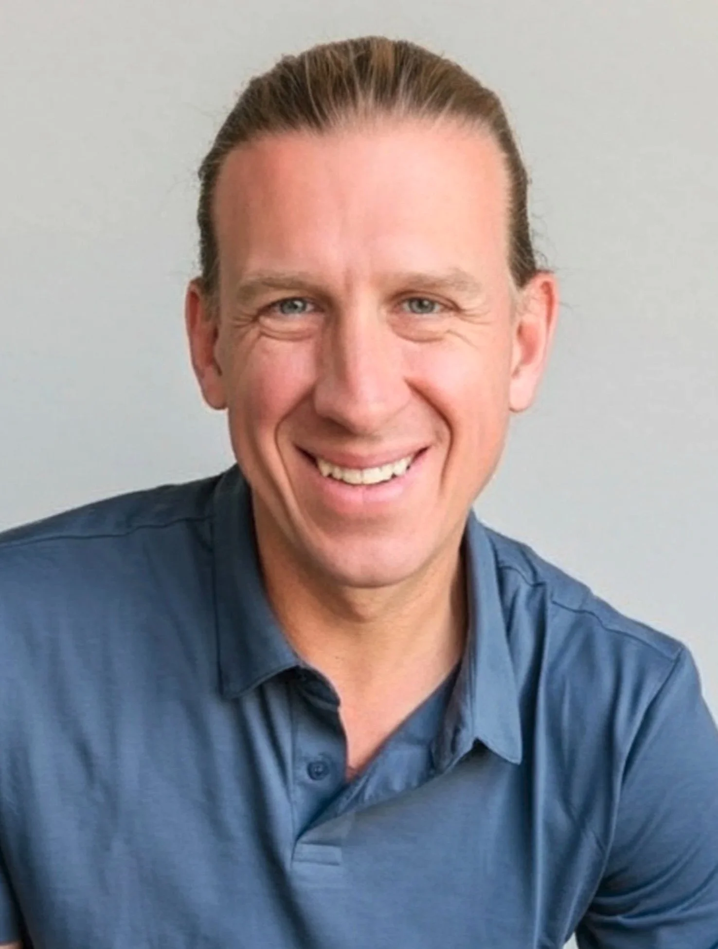 A smiling man with blonde hair and blue eyes, wearing a black shirt, against a light gray background.