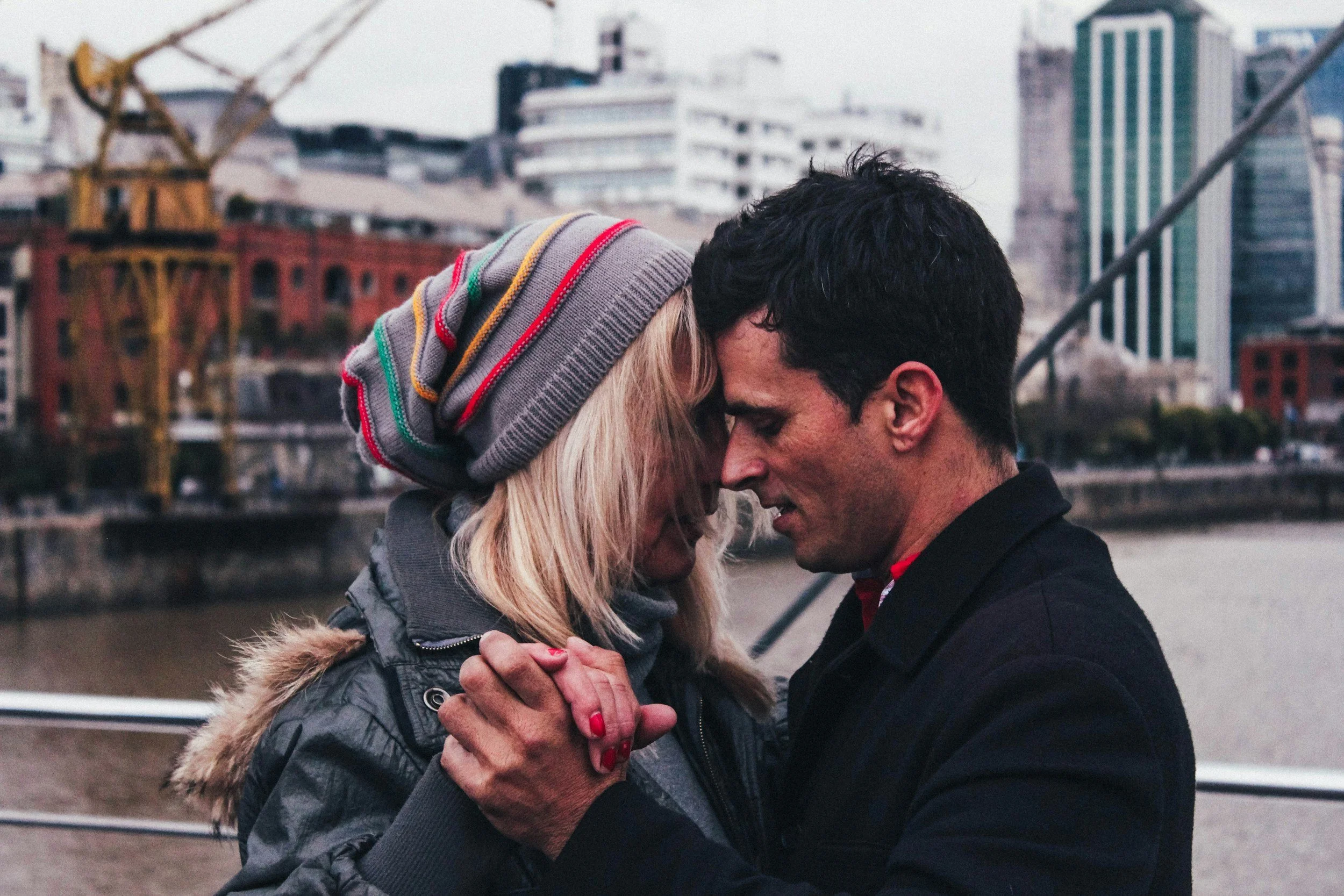 Couple embracing and holding hands outdoors with a city skyline in the background