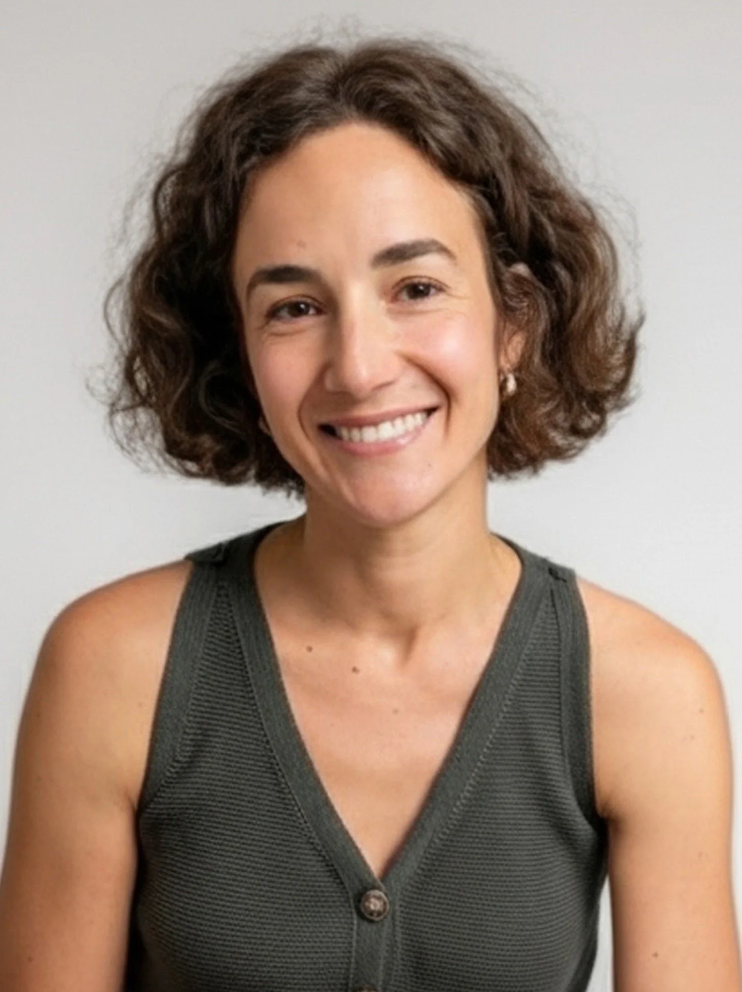A woman with short, curly dark hair, smiling and winking, wearing a dark green collared shirt with vertical stripes against a white background.