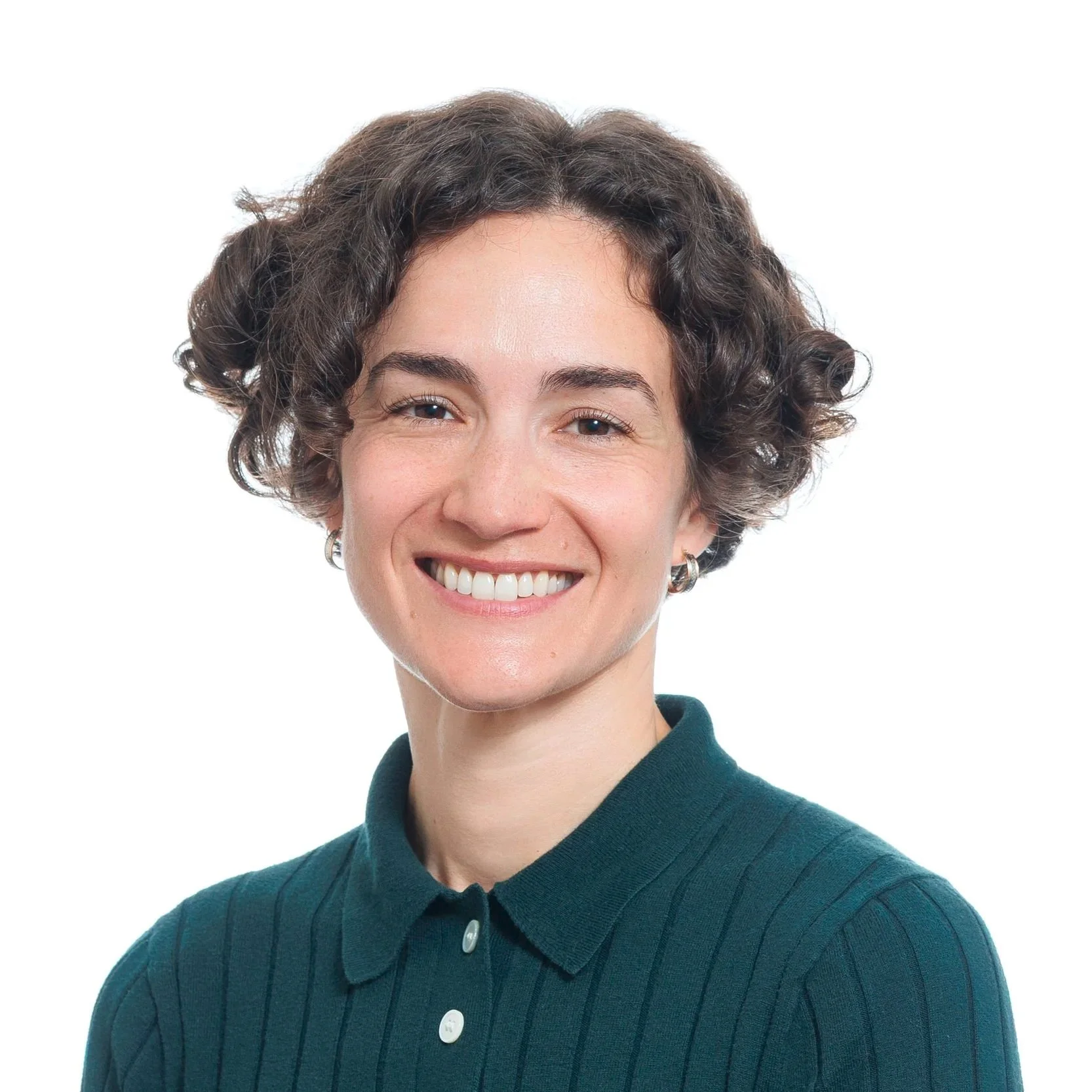 A smiling woman with curly brown hair wearing a dark green collared shirt against a white background.