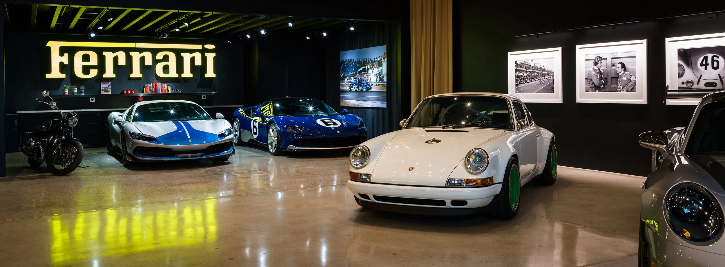 A collection of luxury racing cars - Porsche, Ferrari and a BMW motorcycle displayed in a showroom with a Ferrari sign in the background.