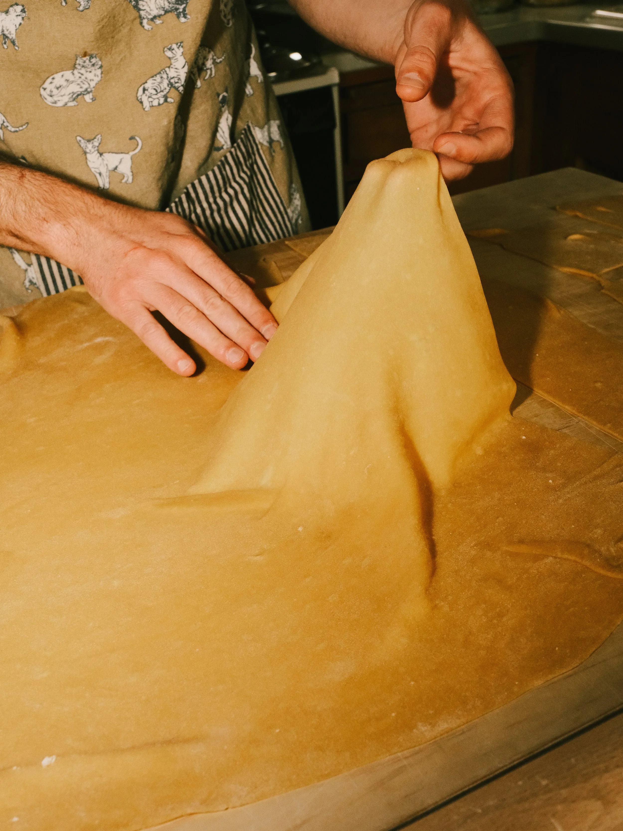 Person folding a large sheet of caramel-colored butterscotch candy on a wooden table.