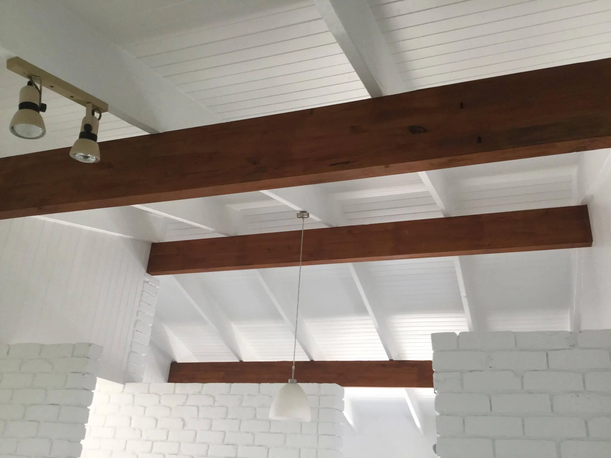 Interior ceiling with white painted brick walls, wooden beams, and ceiling lights.