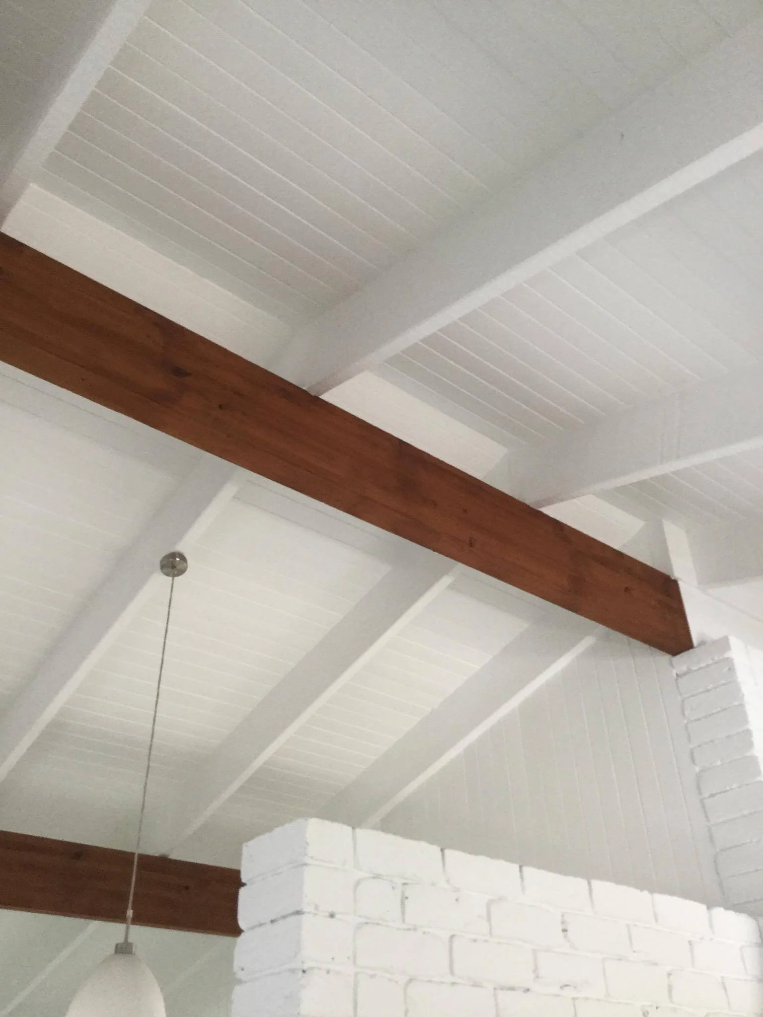 White painted ceiling with exposed wooden beams, white brick pillar, and a hanging light fixture.