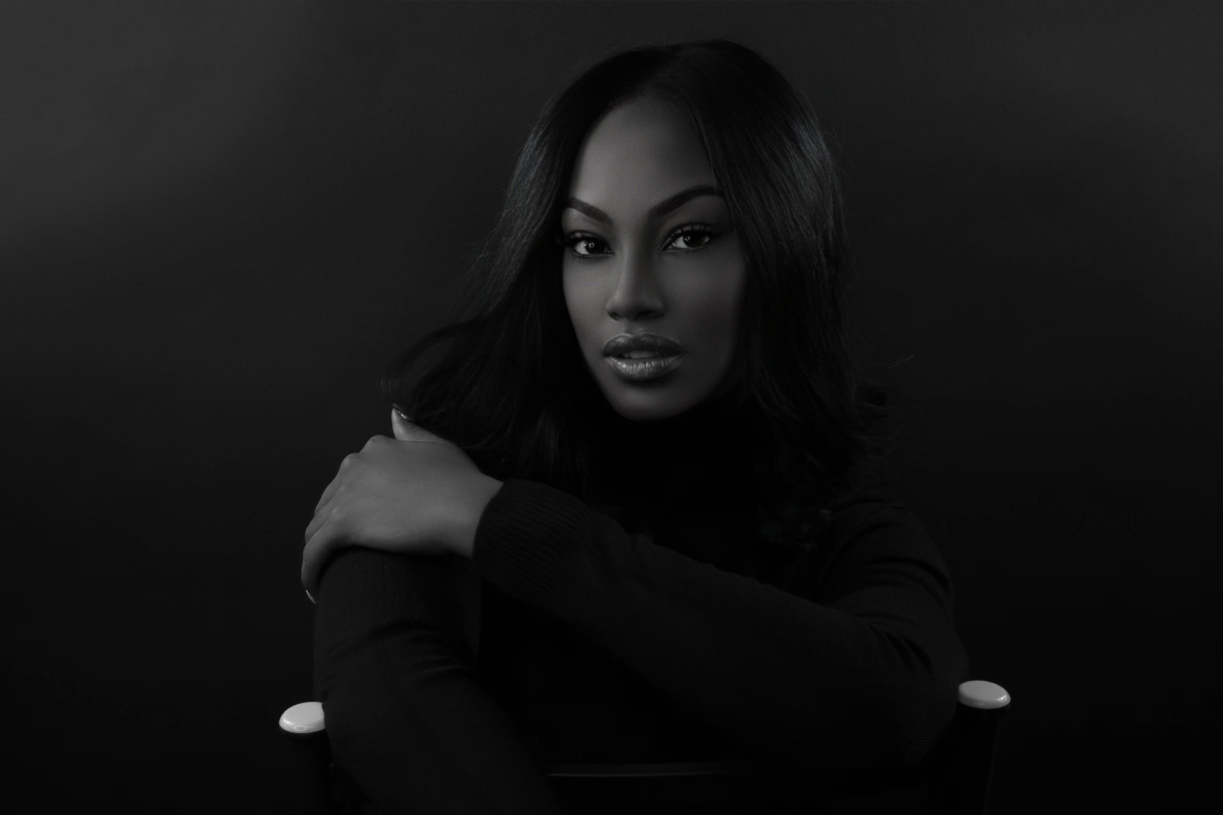 Black and white portrait of a woman with dark hair, looking directly at the camera with her hand resting on her shoulder.